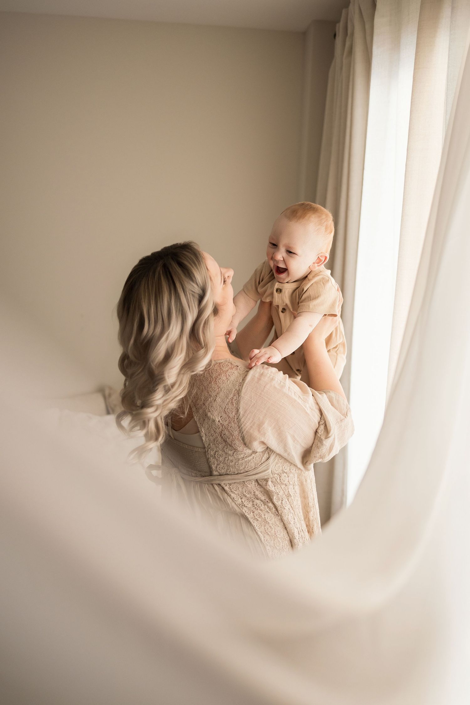 A series of soft, ethereal photos showing a figure in beige holding a baby against a light window background.