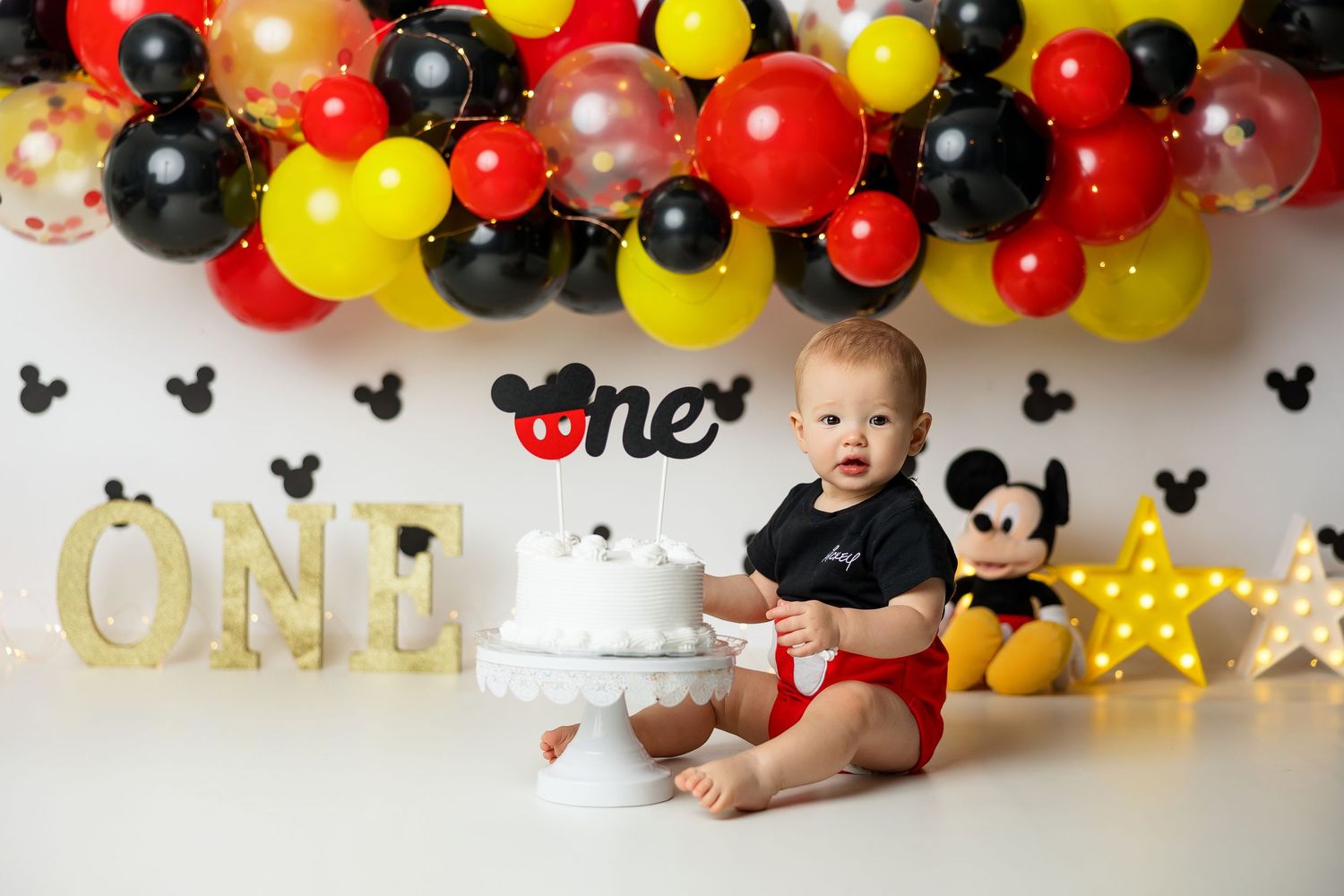 Mickey Mouse themed first birthday party decorations with black, red, and yellow balloons and star accents.