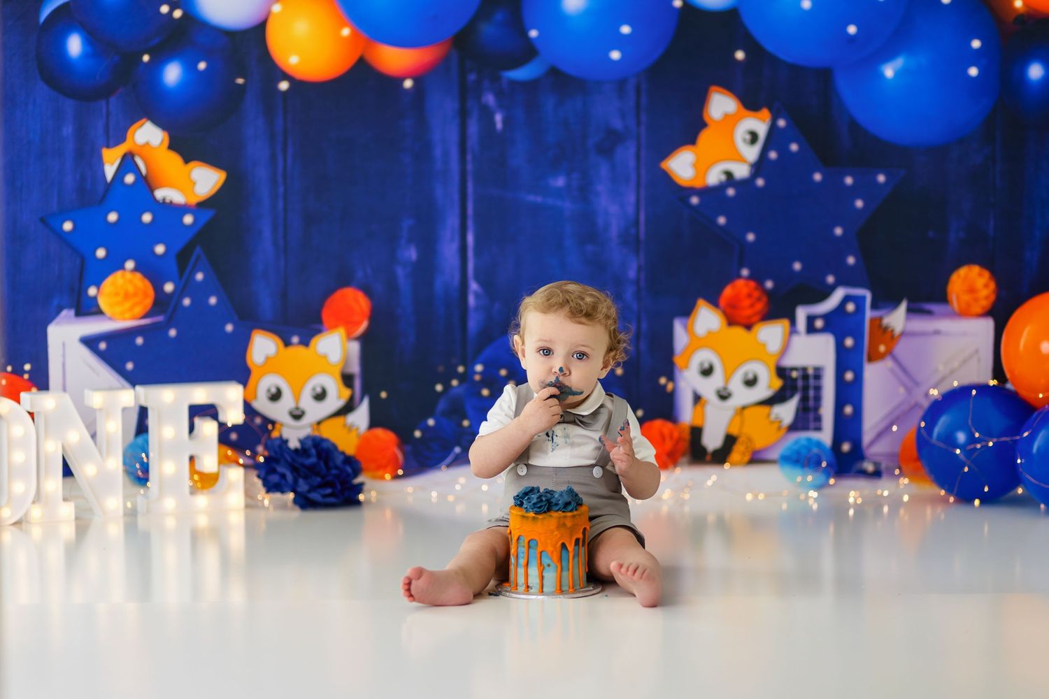 Birthday party setup with blue and orange balloons, teddy bear decorations, and white lettering against a blue backdrop.