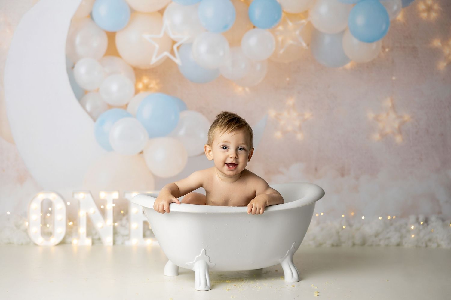 Professional portrait session in soft pastel colors with clouds, balloons and a vintage bathtub against dreamy backdrop.
