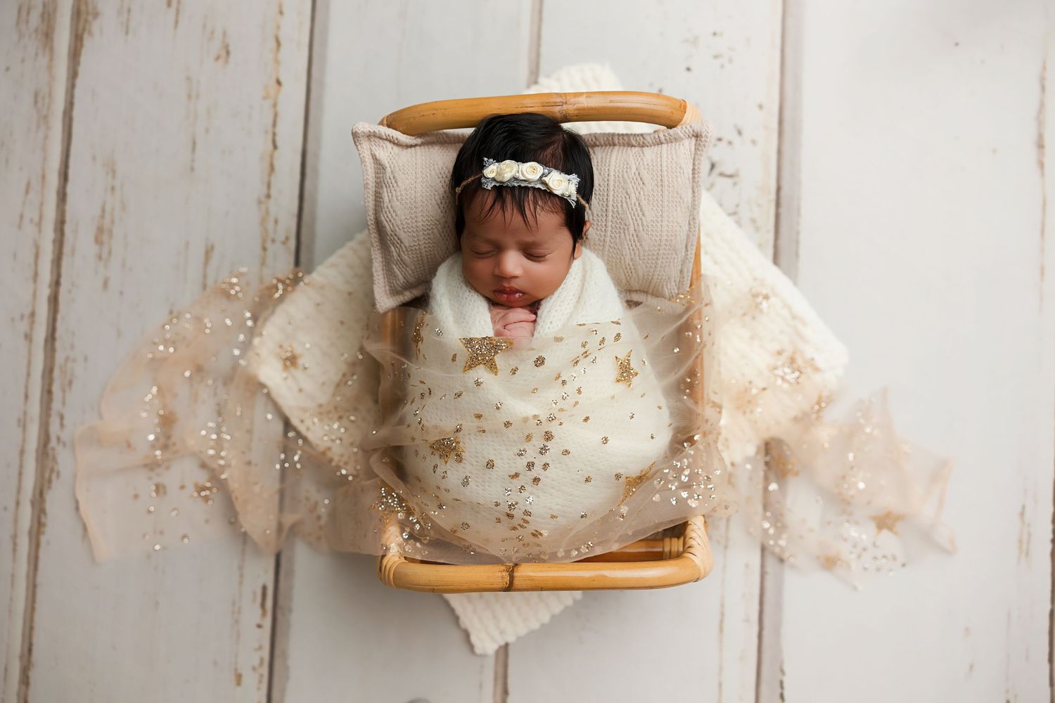 Sleeping newborn in white wrap positioned in wooden basket with delicate lace overlay.