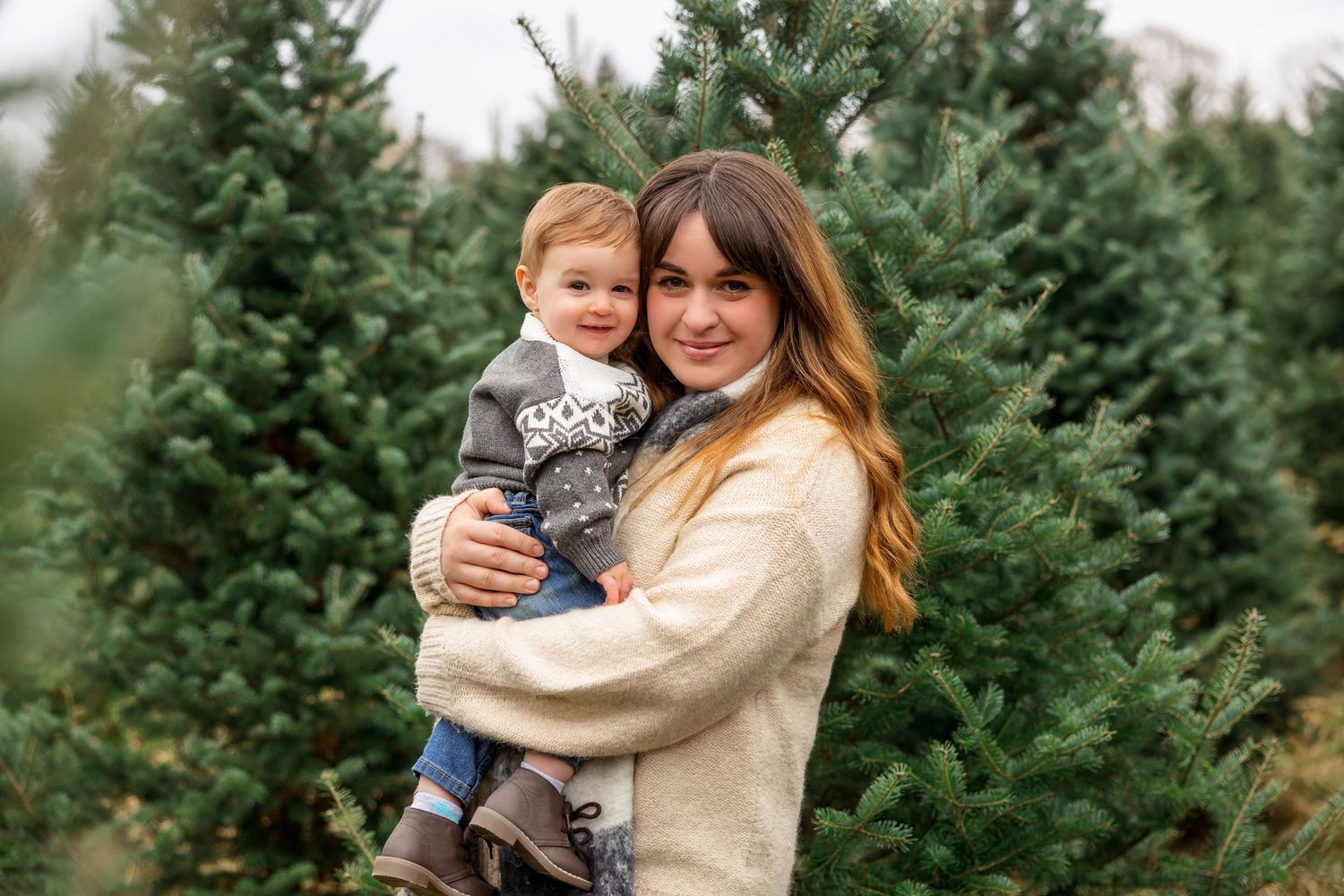 Mother and child embracing at a Christmas tree farm on a winter day.