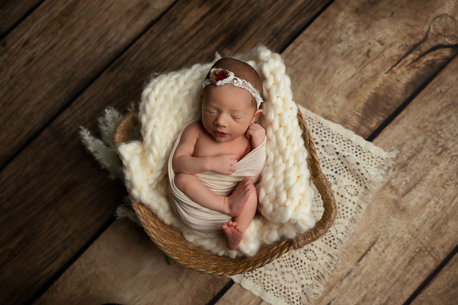 Sleeping newborn wrapped in white blanket in rustic wooden basket.