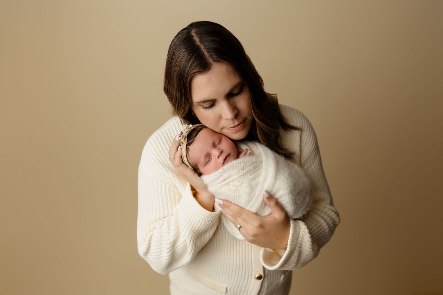Intimate moment between parent and newborn wearing white sweater against beige background.