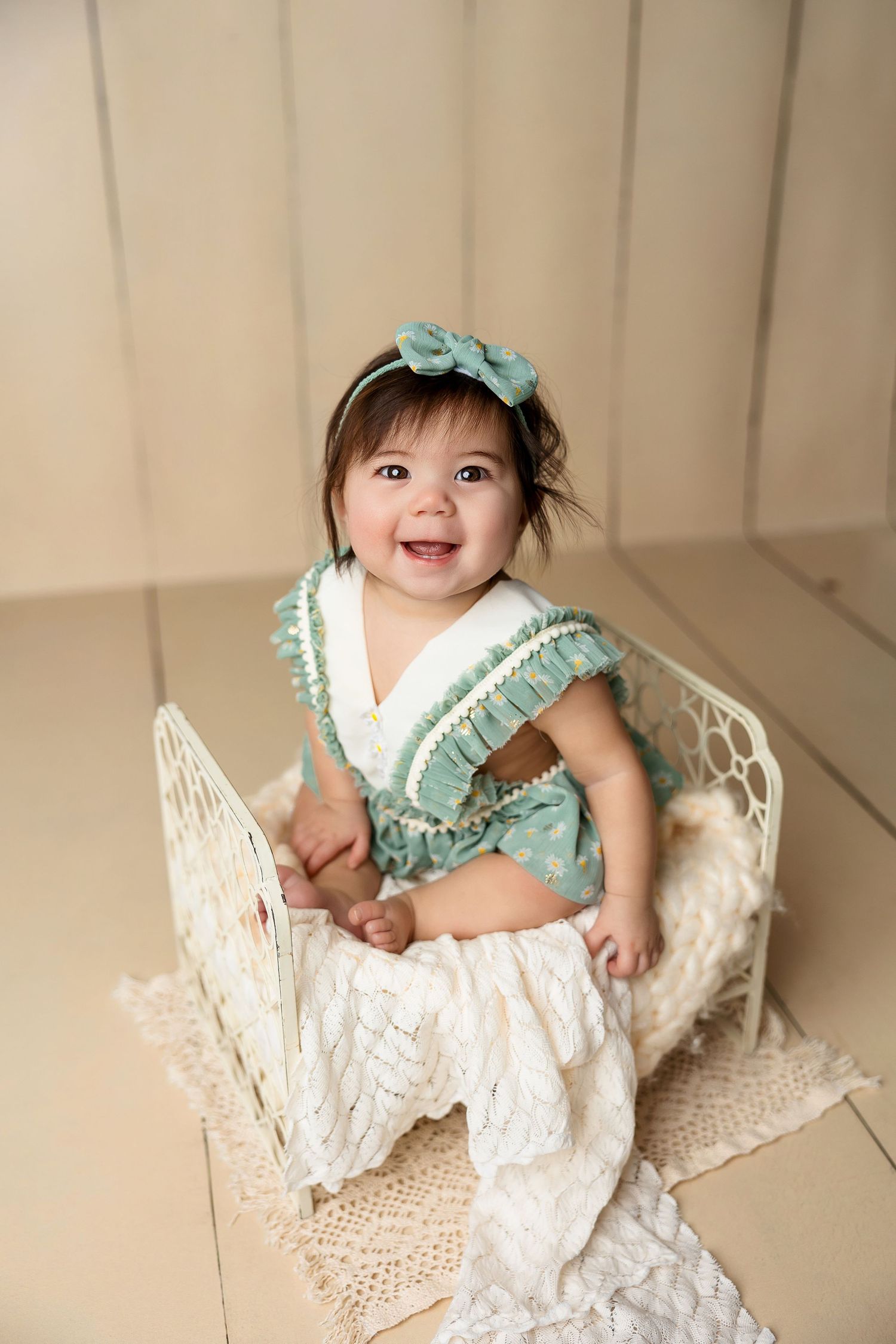 Baby in mint outfit sitting on lace-decorated chair during studio photoshoot.