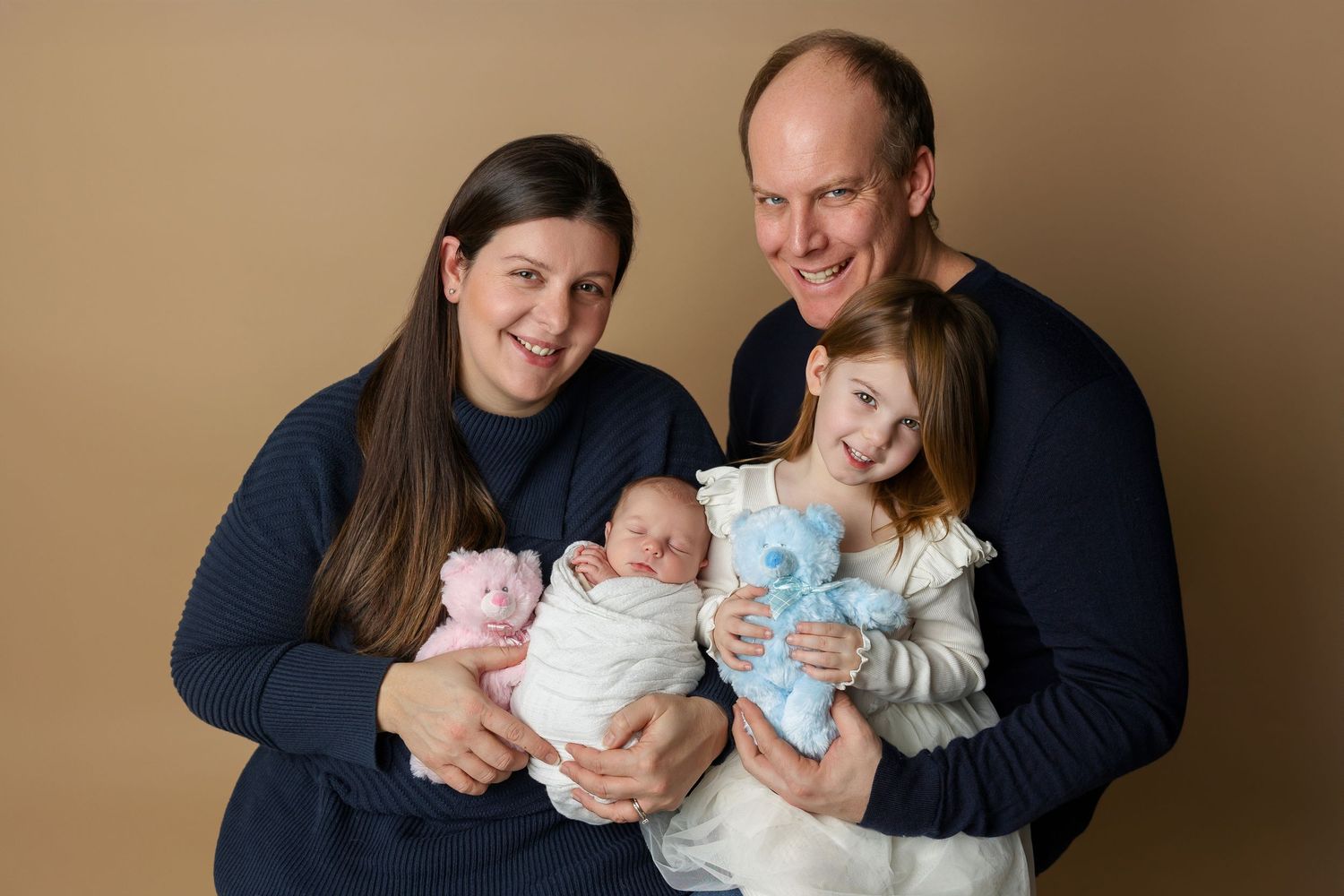 A loving couple sits together holding their newborn twins in a heartwarming family portrait session.