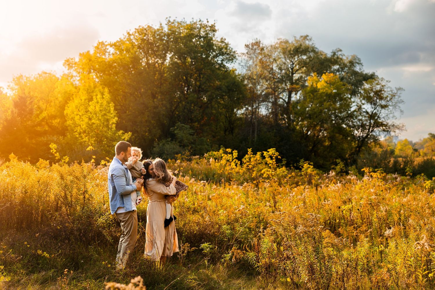 A couple stands in a golden meadow at sunset with wildflowers blooming around them.