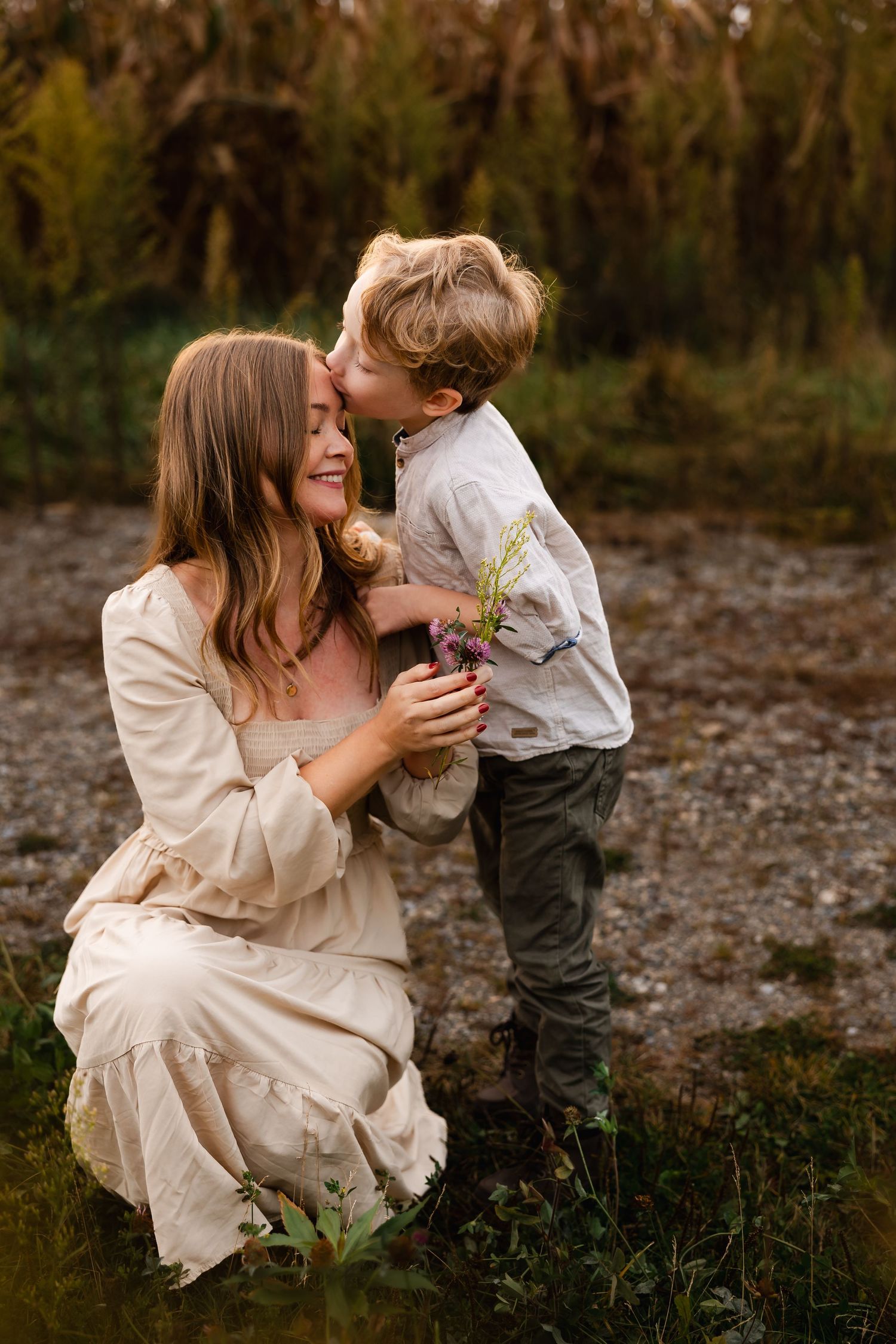 Mother and child share tender playful moments outdoors on a rocky beach at sunset.