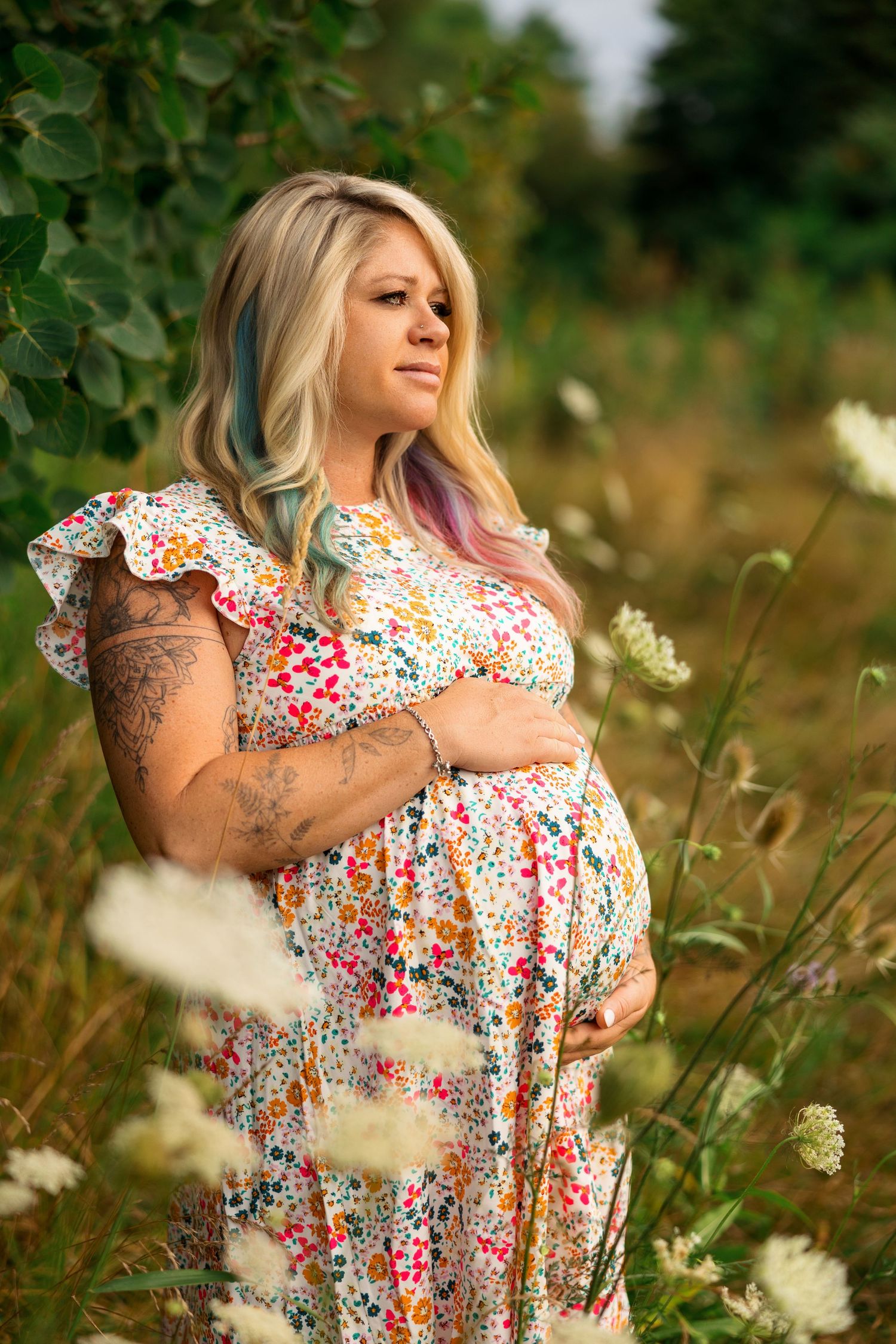 A person wearing a floral print dress poses in a field of wild flowers and tall grass during golden hour.