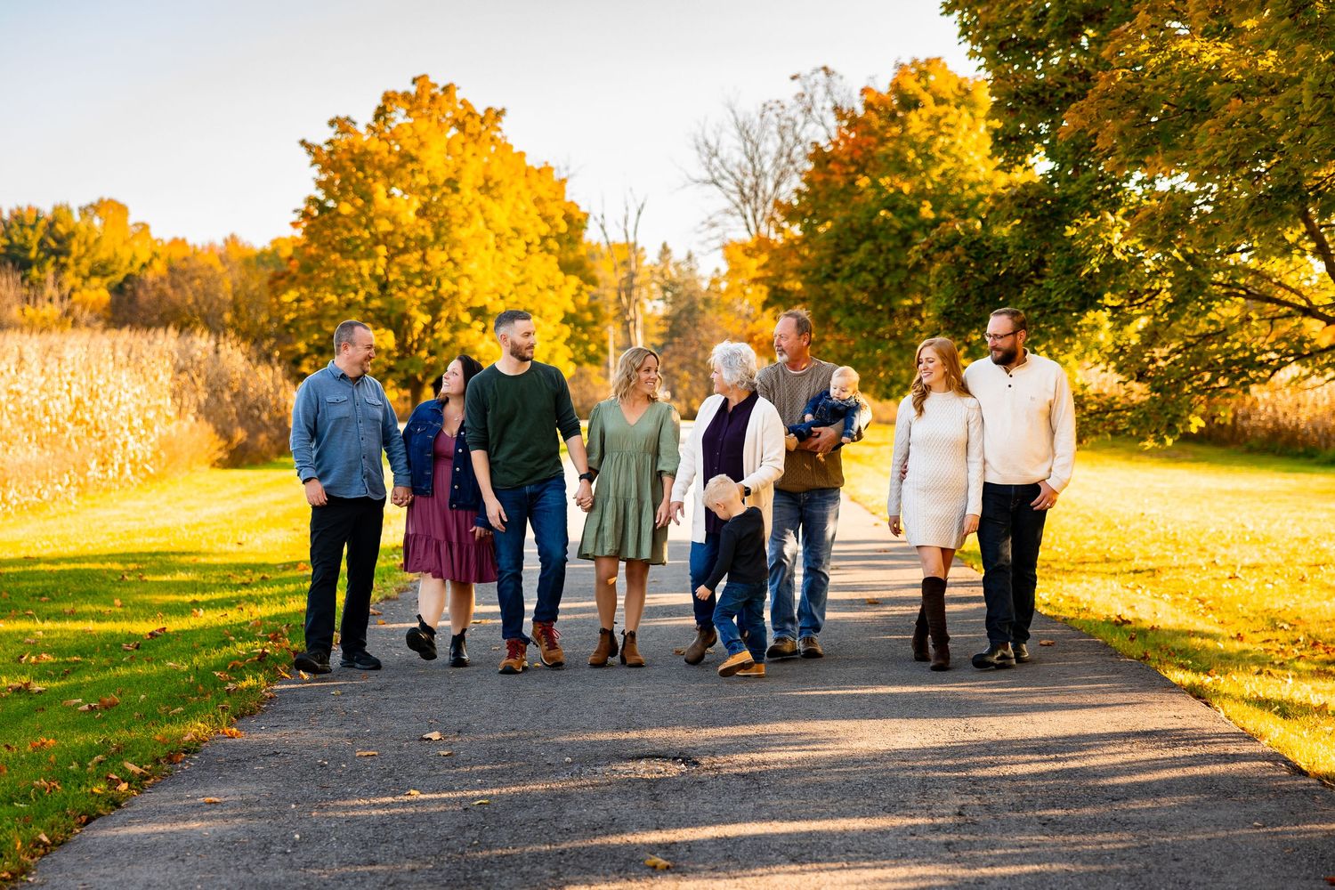 Multi-generational family walking together on a tree-lined path during colorful autumn foliage season.