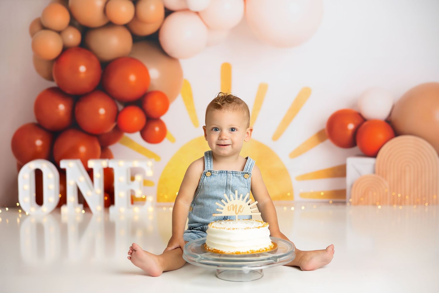 First birthday cake scene with balloon decorations and yellow sun backdrop.