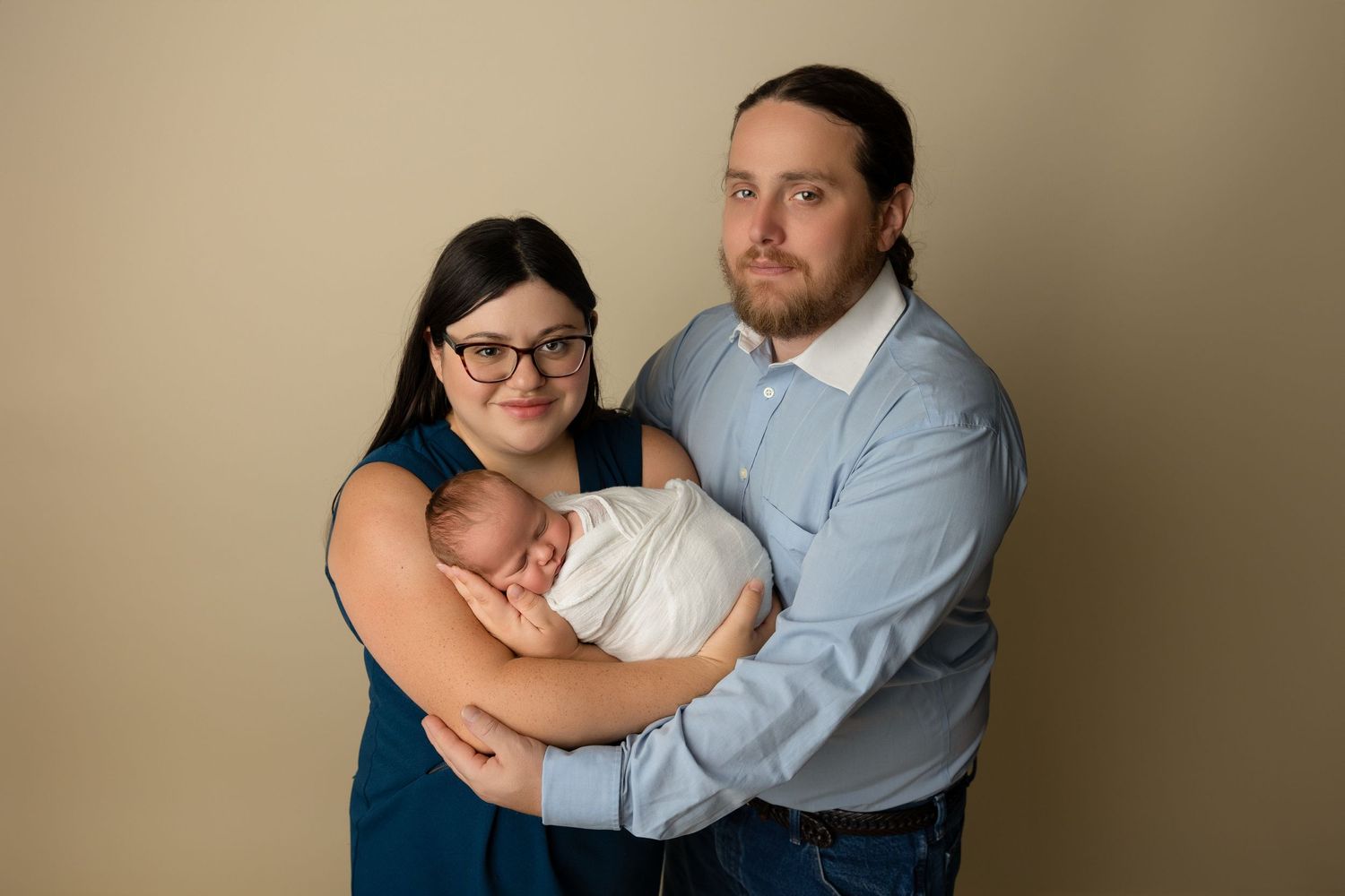 Studio family portrait against beige backdrop with coordinated blue and white outfits.