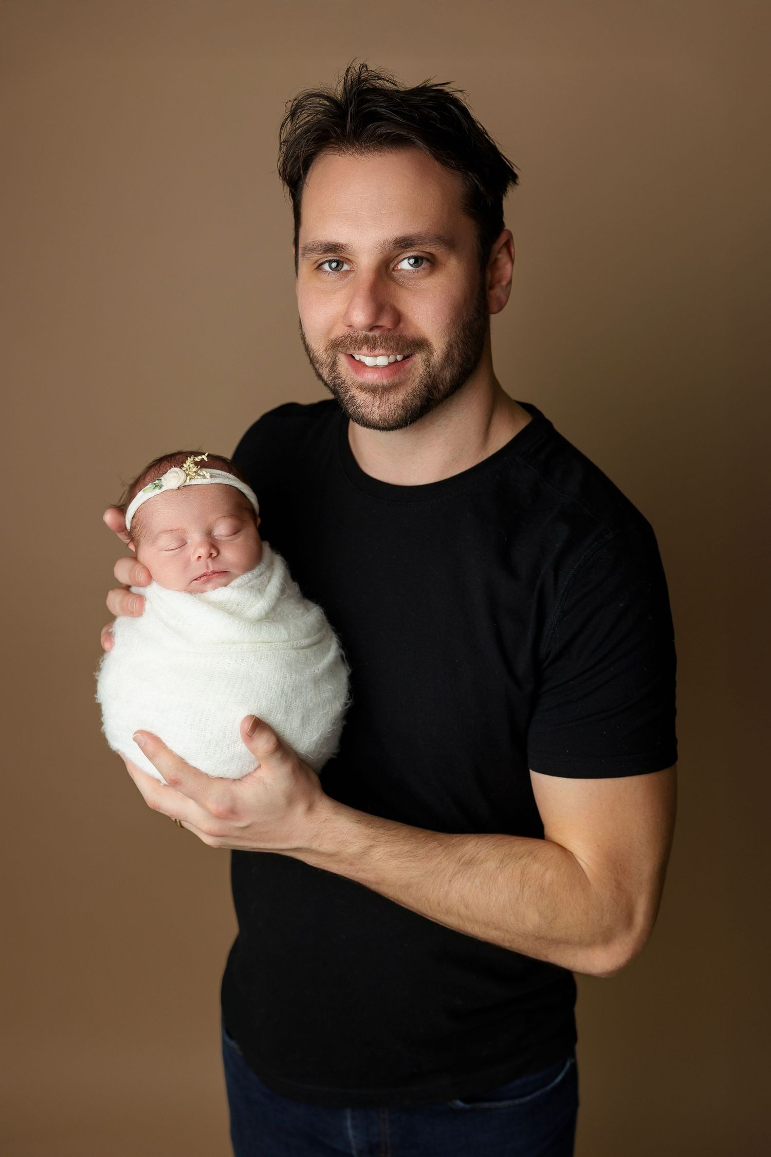 Studio portrait with swaddled newborn against warm brown background.