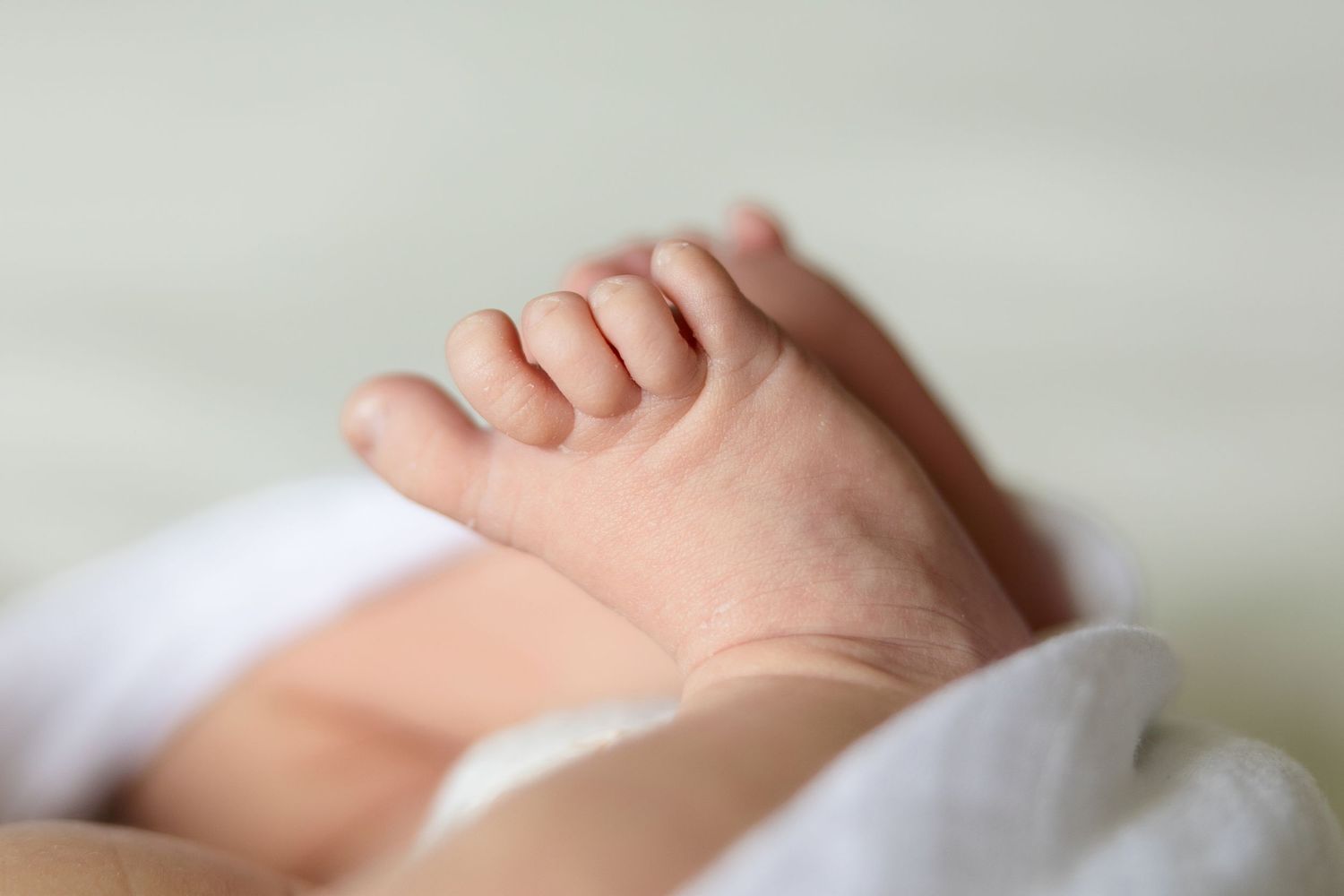 A tiny baby foot rests peacefully on soft white bedding, showcasing delicate toes against a light background.