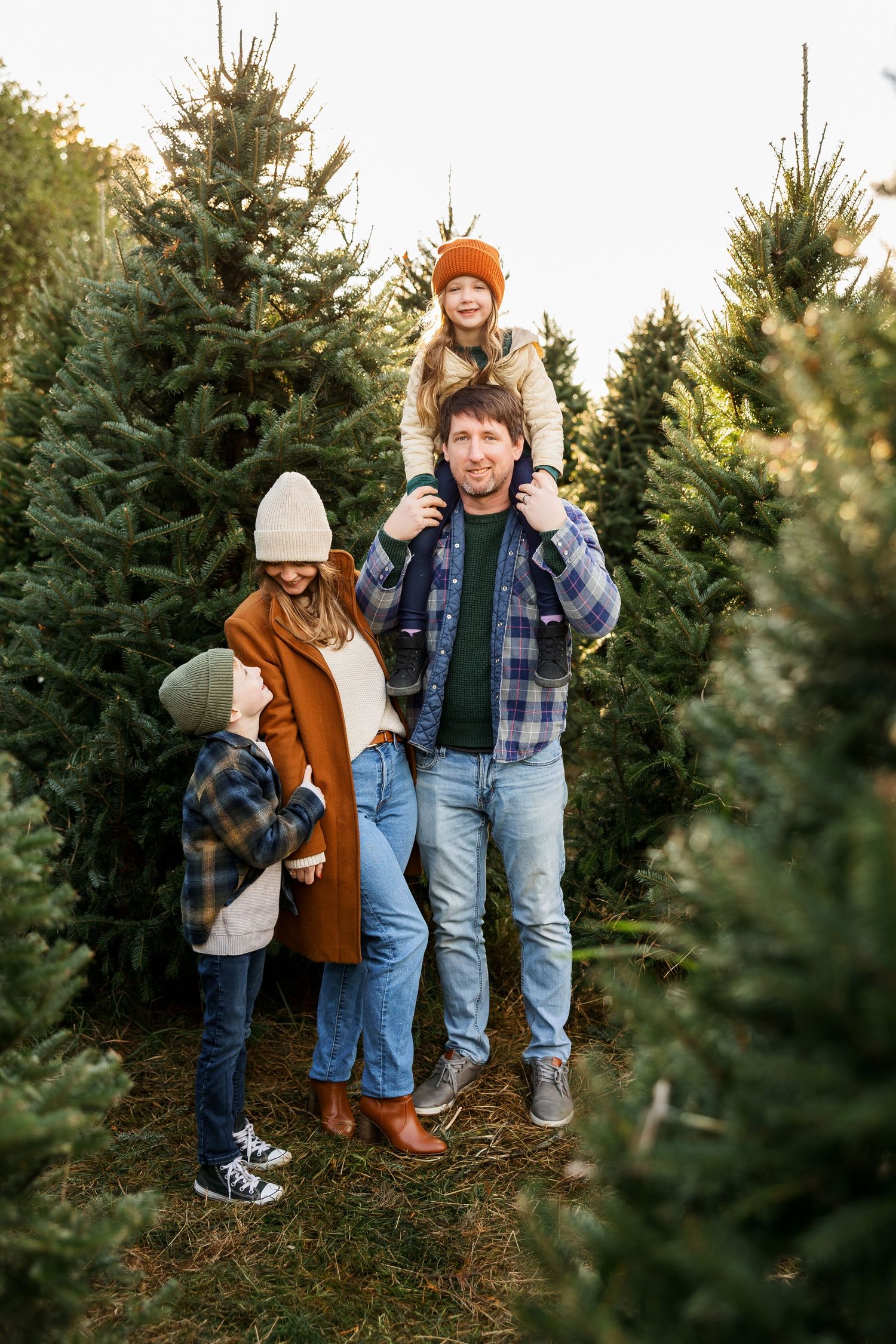 Family wearing winter clothing shops for a Christmas tree together at an evergreen tree farm.