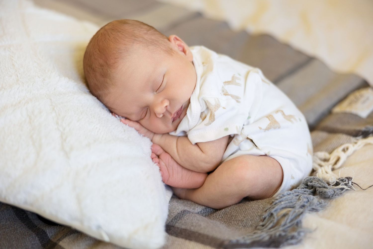 A sleeping newborn baby wrapped in soft white fabric lying peacefully on a light-colored surface.