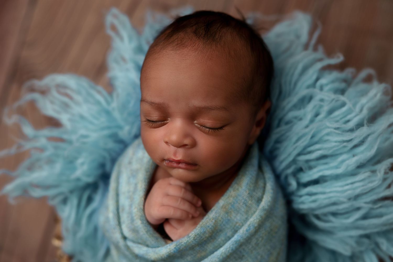 Peaceful sleeping newborn swaddled in light blue fabric against turquoise textured backdrop.