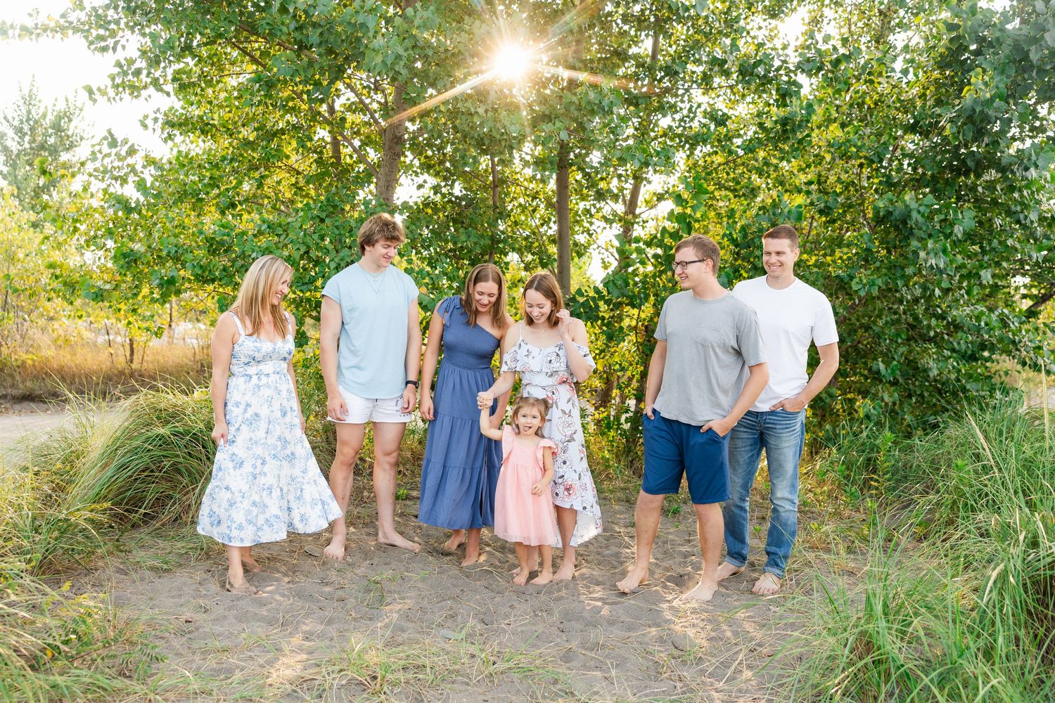 A group stands together on a sunlit path outdoors with trees and tall grass during golden hour.