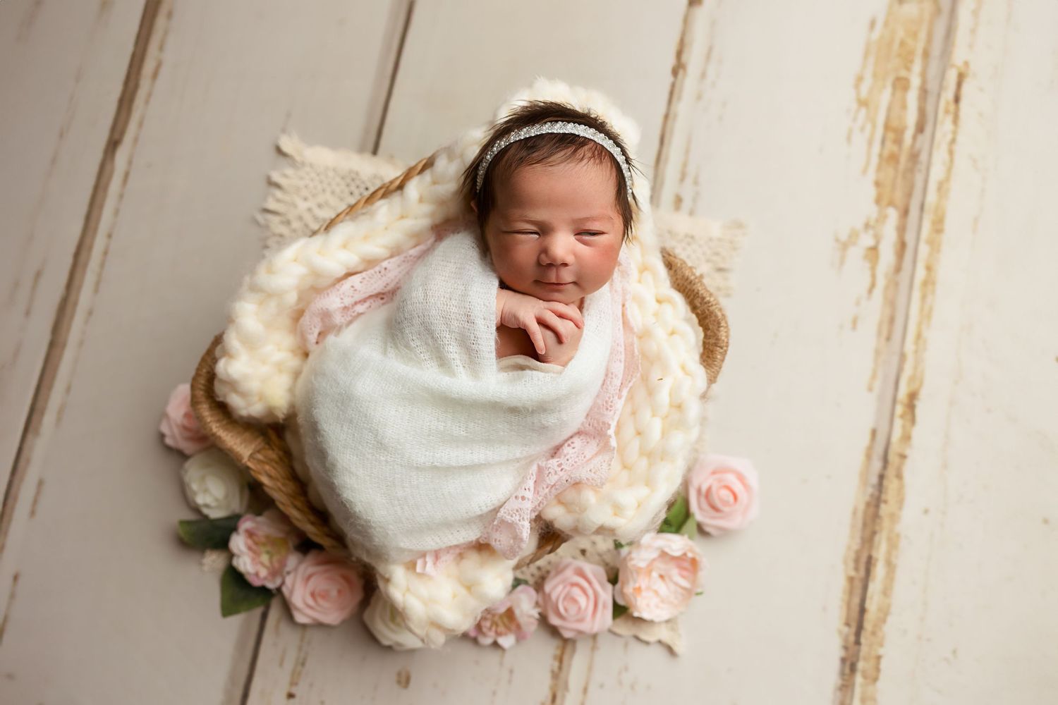 Newborn baby sleeping peacefully surrounded by pink roses on vintage wood background.