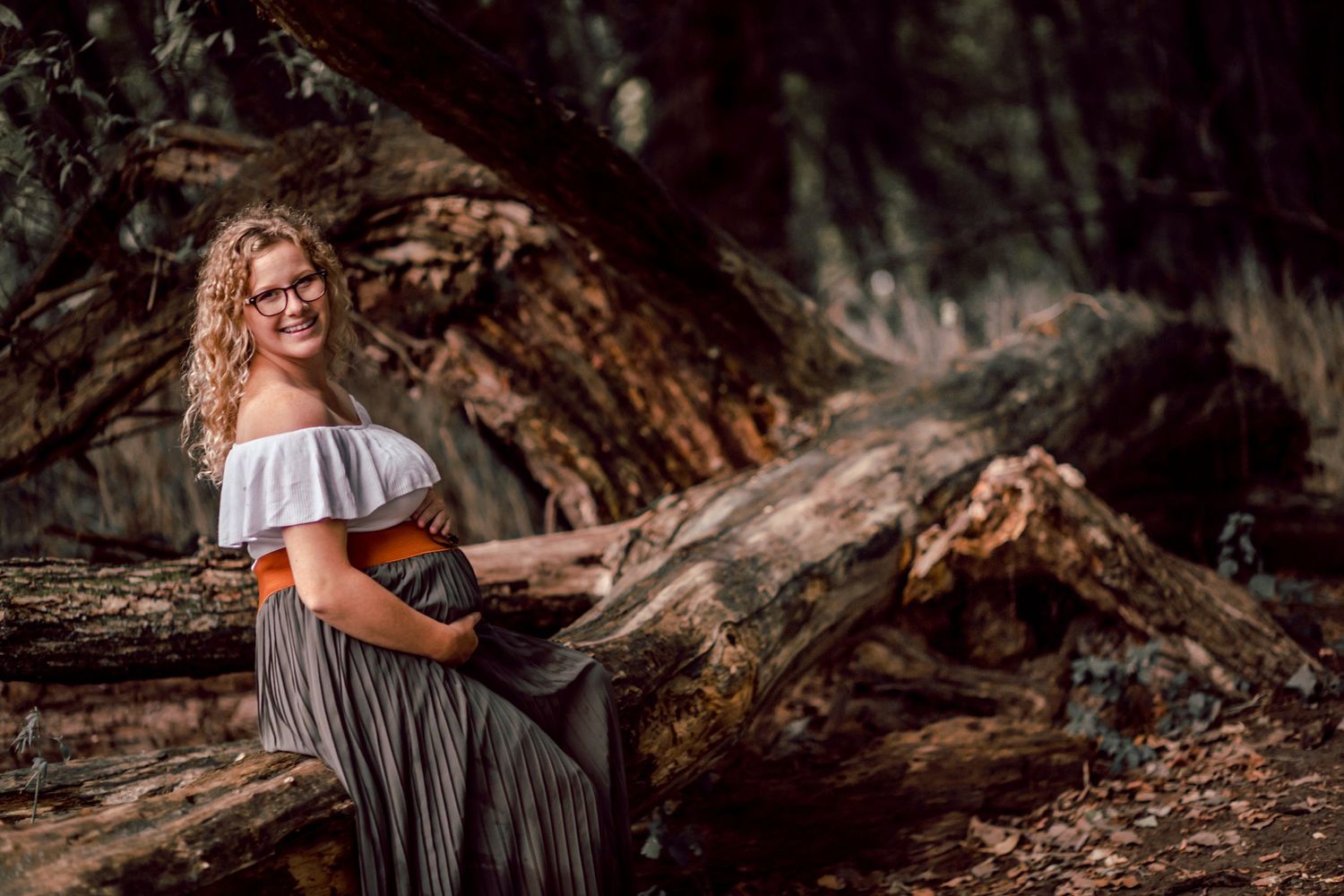 A musician plays guitar while sitting on fallen logs in a dreamy forest setting.