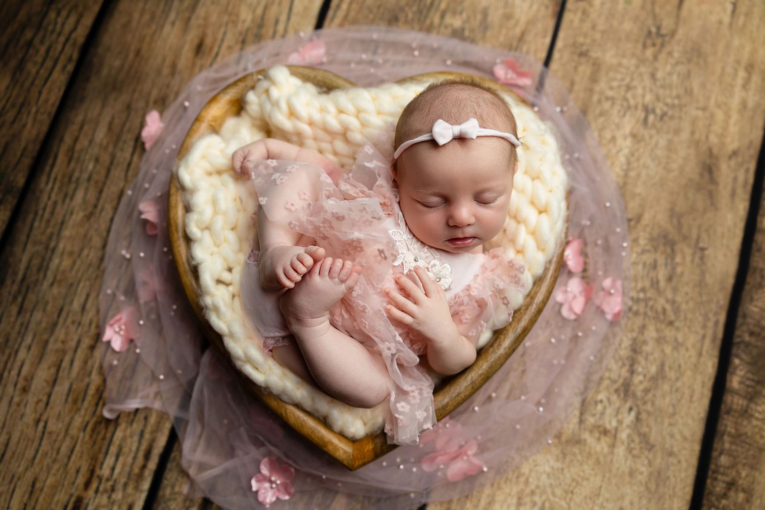 Rustic wooden backdrop with a cozy cream blanket arranged in a bowl for infant photography.