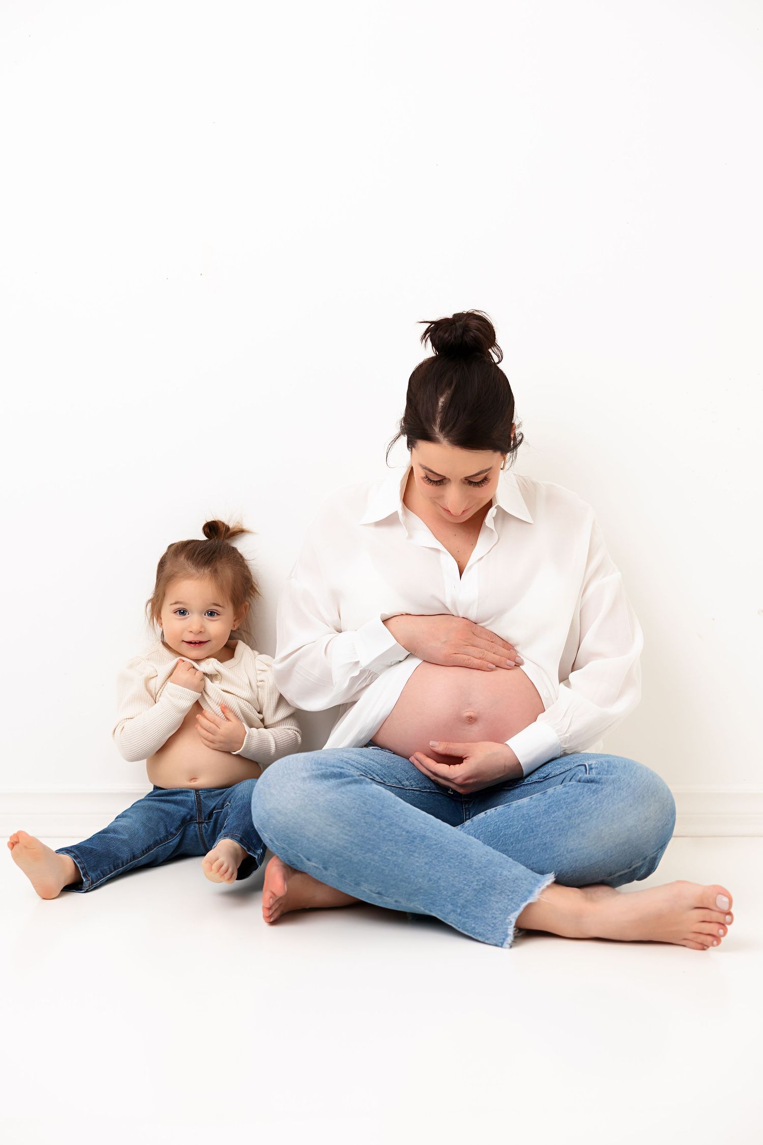 Intimate family moment against white backdrop as toddler and mother share tender moment.