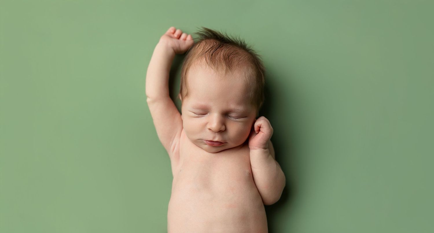 Newborn baby sleeping on green background with stretched arms.