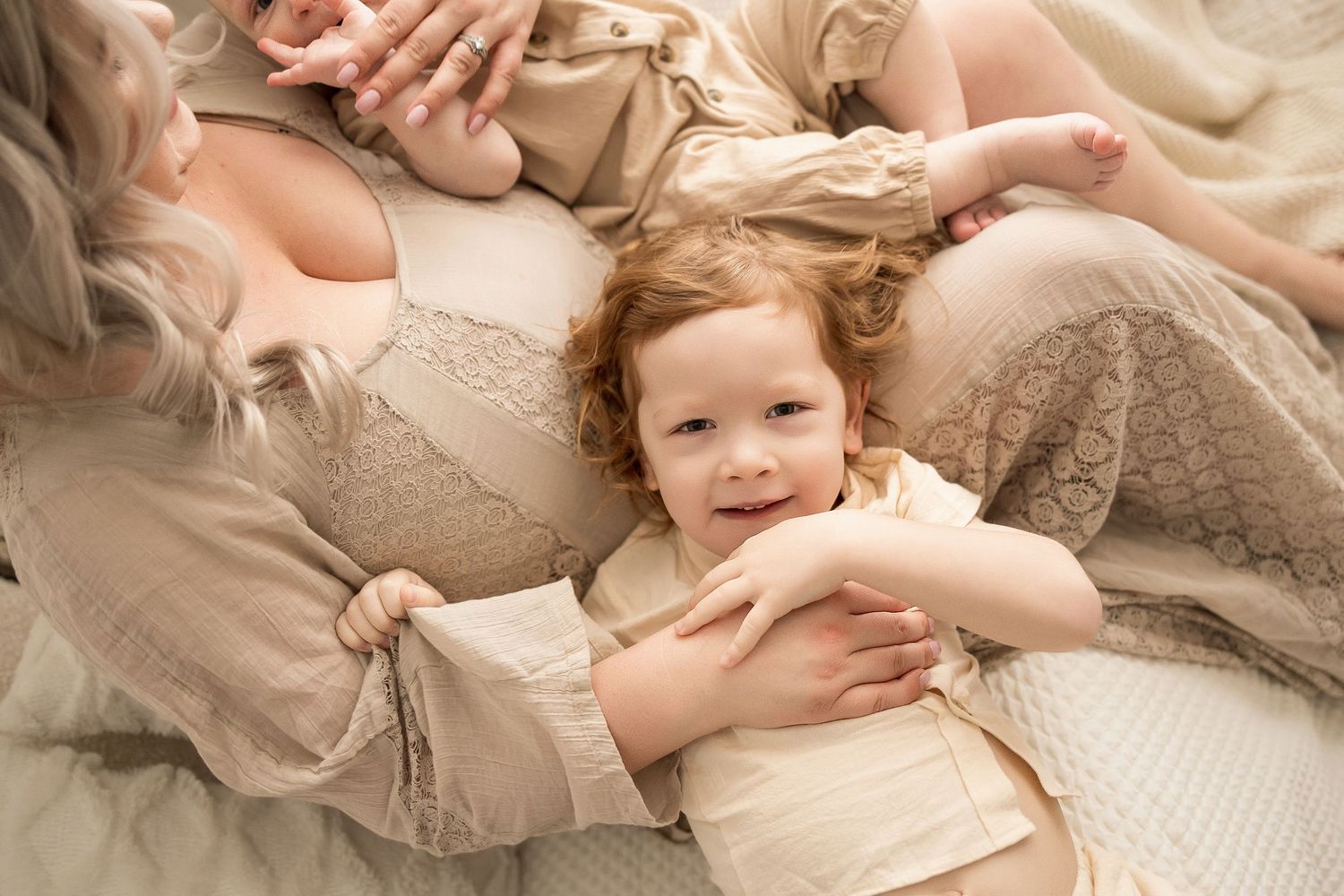 A tender family moment captured on soft beige bedding with gentle natural lighting.