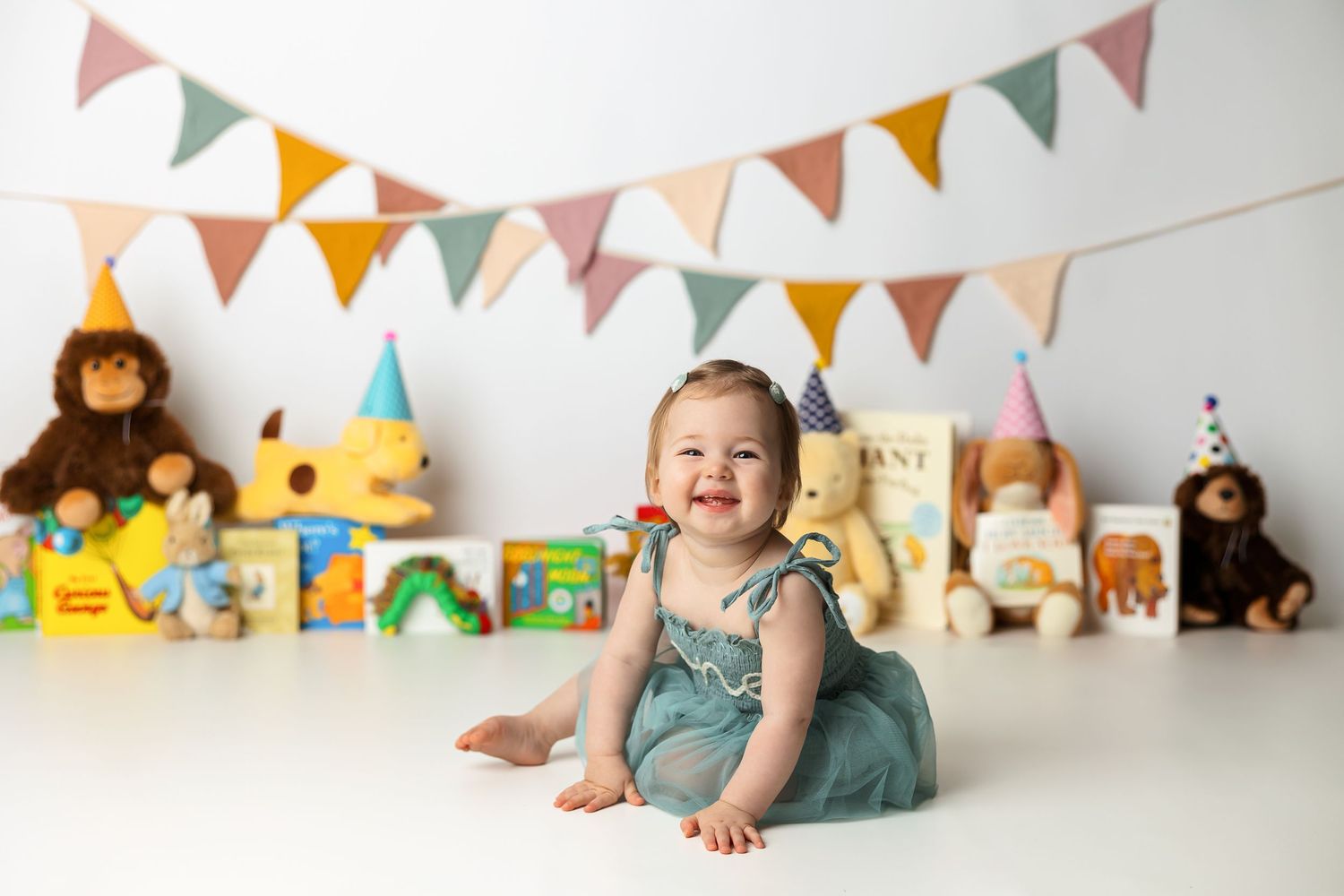 Colorful first birthday scene with bunting flags and stuffed animals displayed on white background.