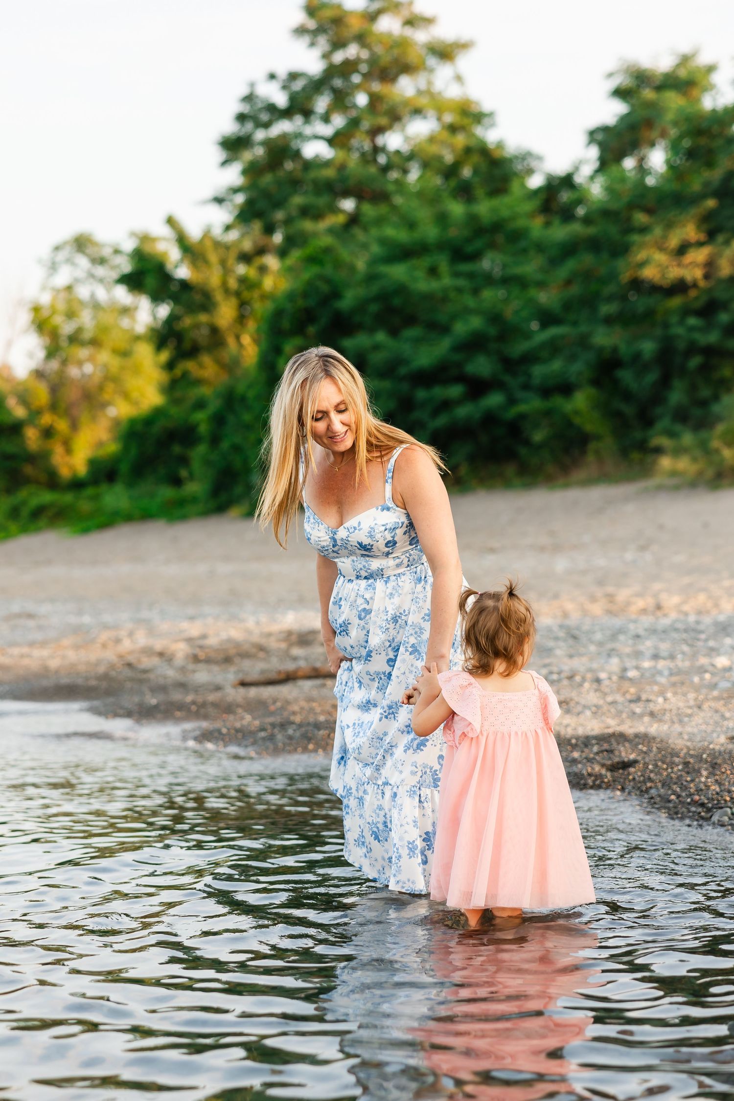 A tender moment captured between two people in floral and pink dresses standing in shallow water at sunset.