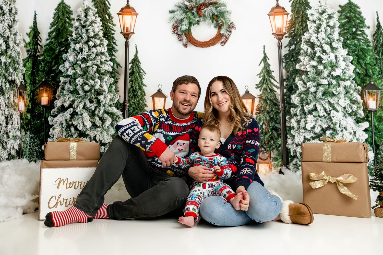 Family in matching Christmas sweaters poses with presents and holiday decorations.