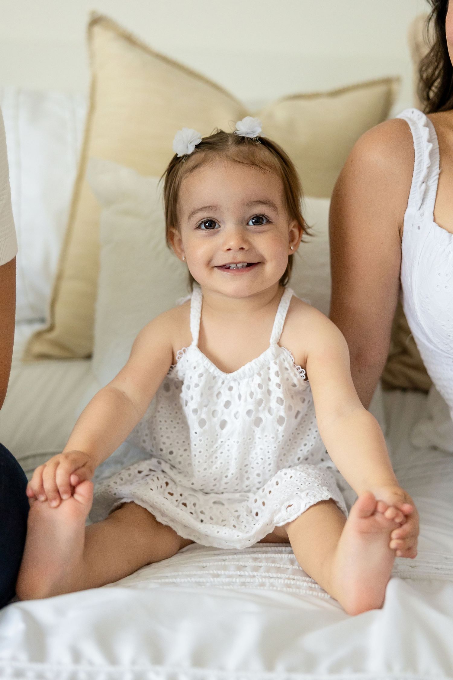 A child wearing white clothing lies on a soft white bedspread displaying various playful poses.