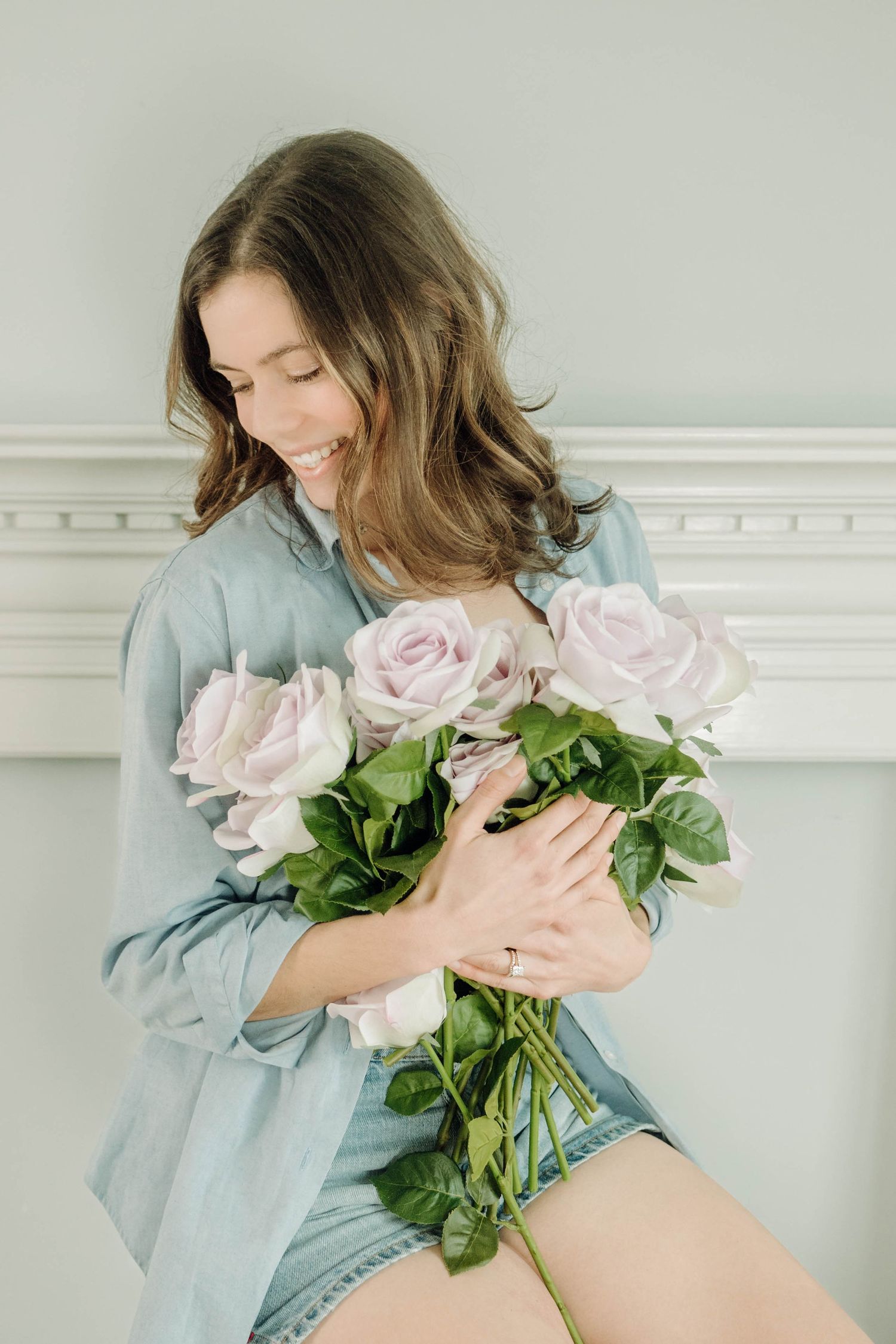 Woman in denim shirt holding beautiful pale pink roses against white wall background.