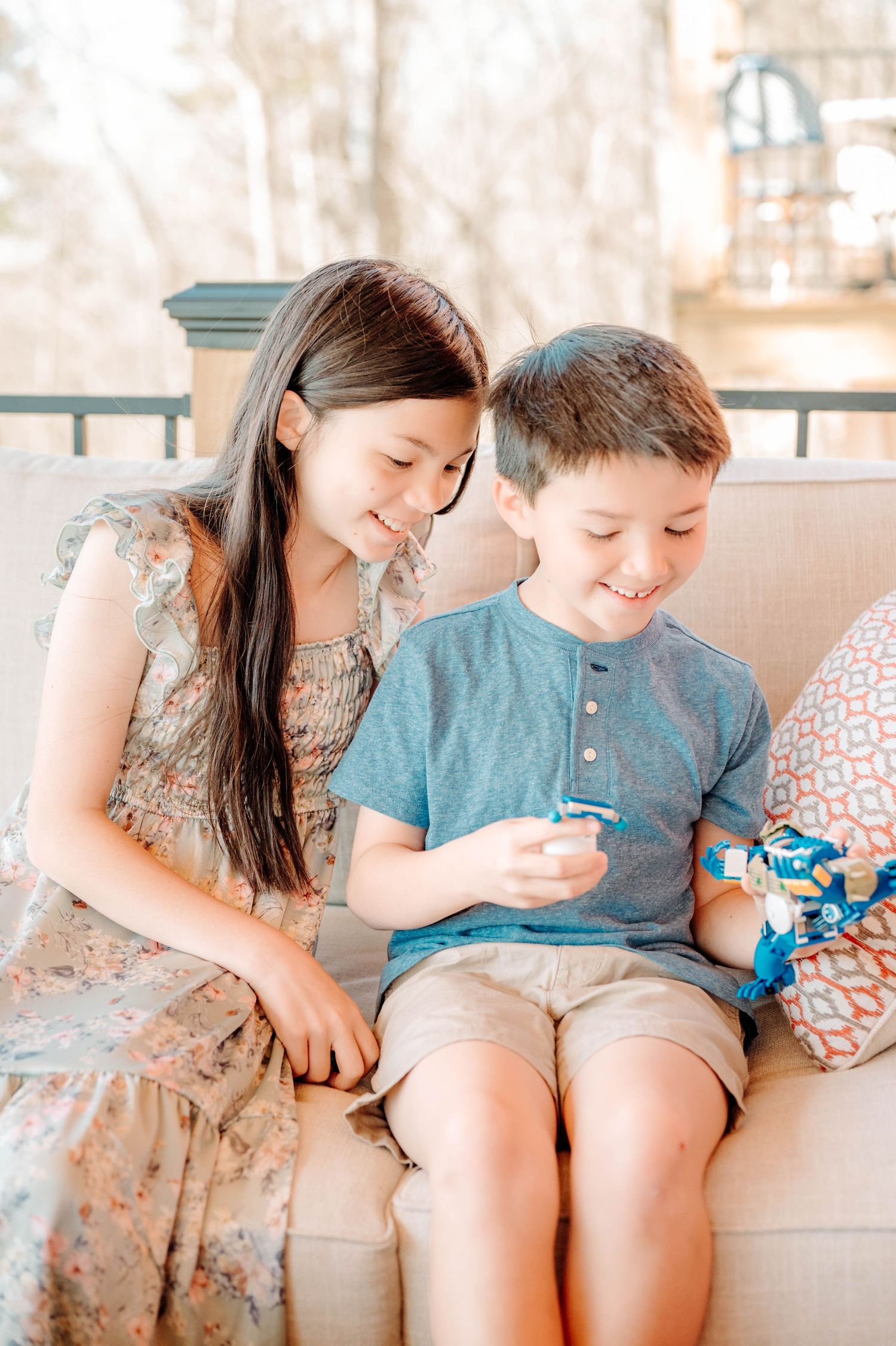 Two children share a happy moment while looking at phone on outdoor porch.