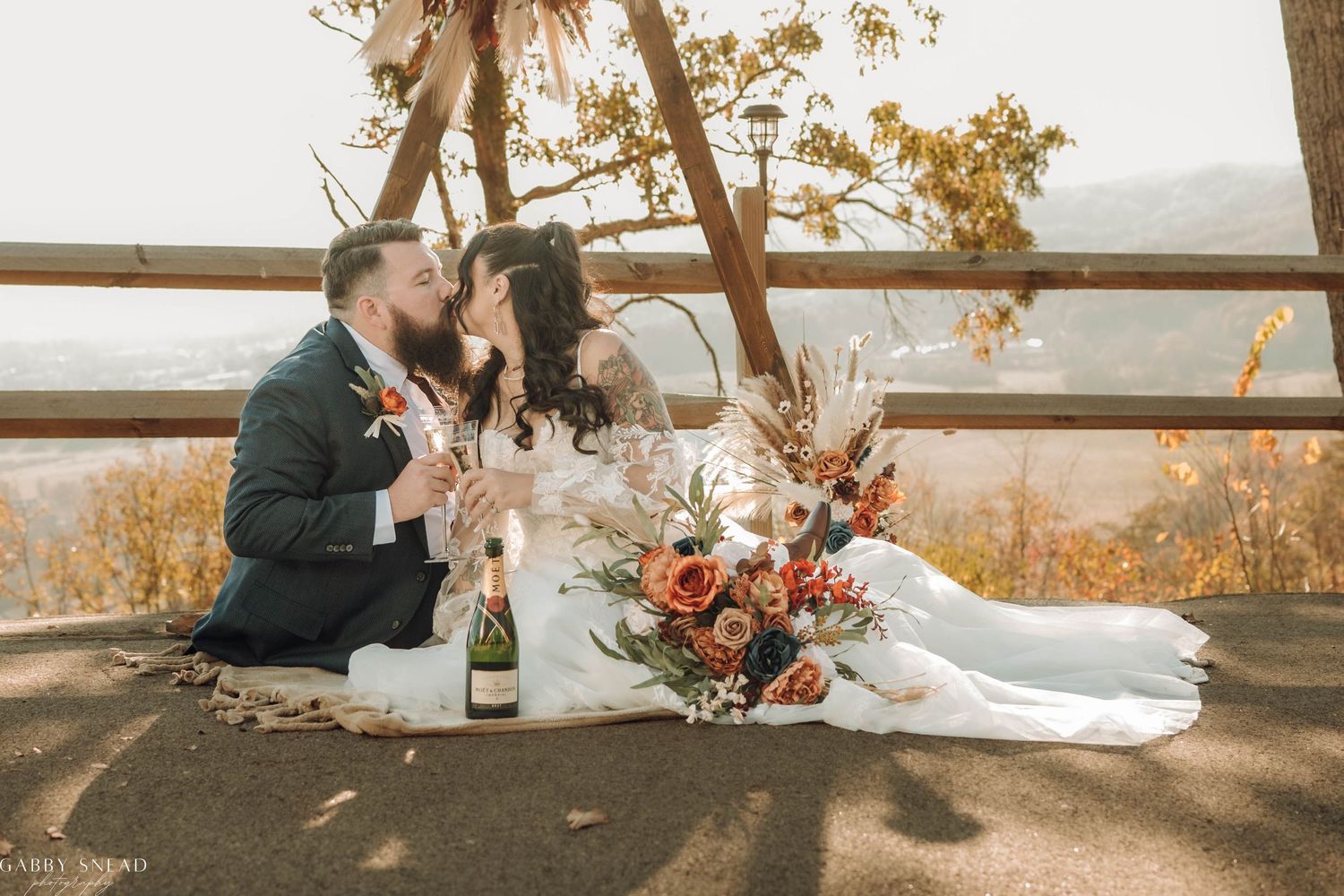 Newlyweds having champagne picnic at scenic overlook during sunset.