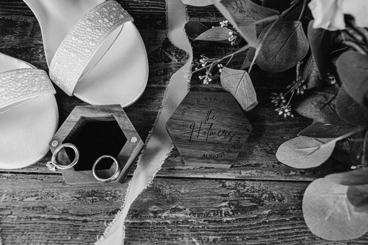 Black and white photo of wedding details including rings and lingerie on wooden surface.