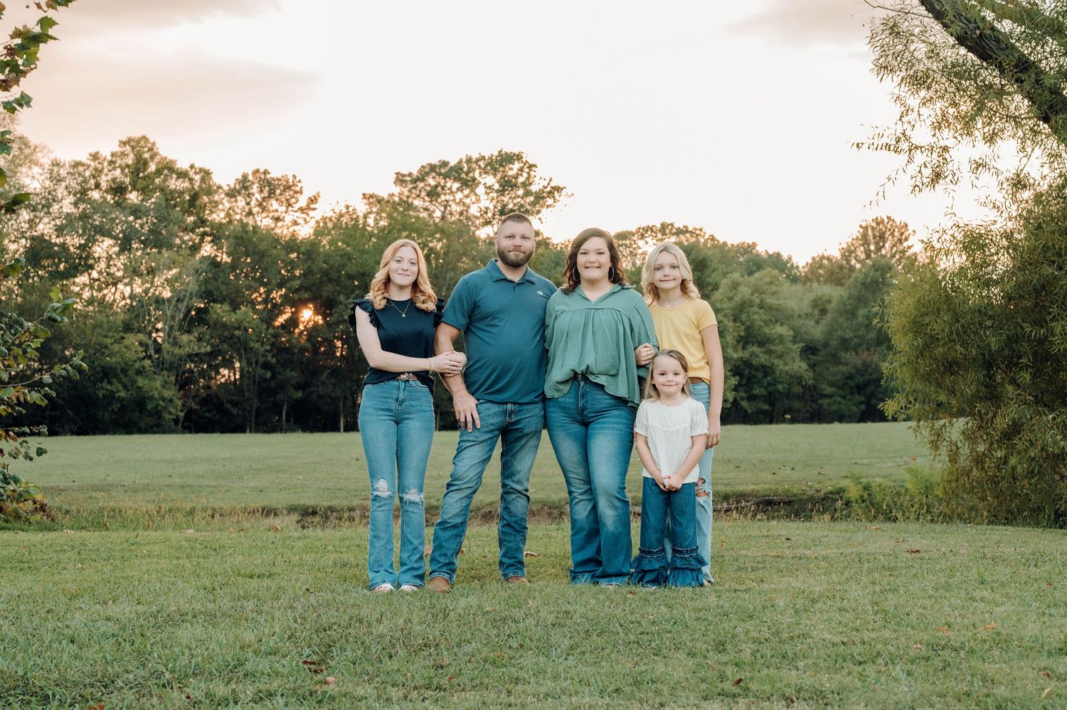 A group of people in coordinating blue and white outfits pose together in a grassy field at sunset.