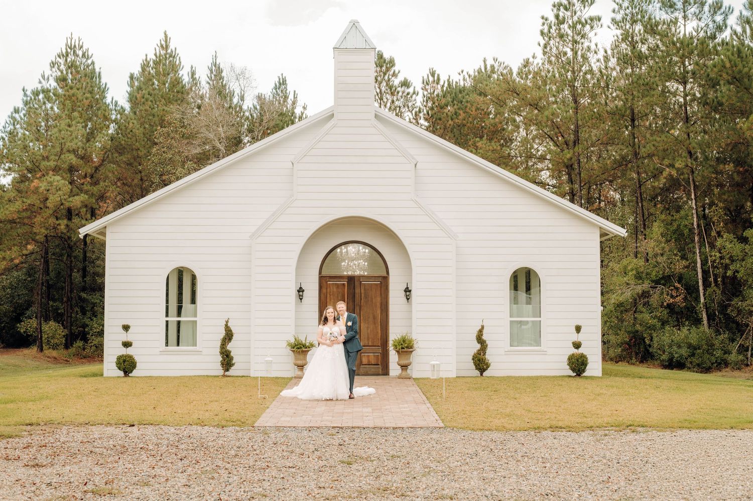 A row of five identical white country churches with steeples surrounded by pine trees and green landscaping.