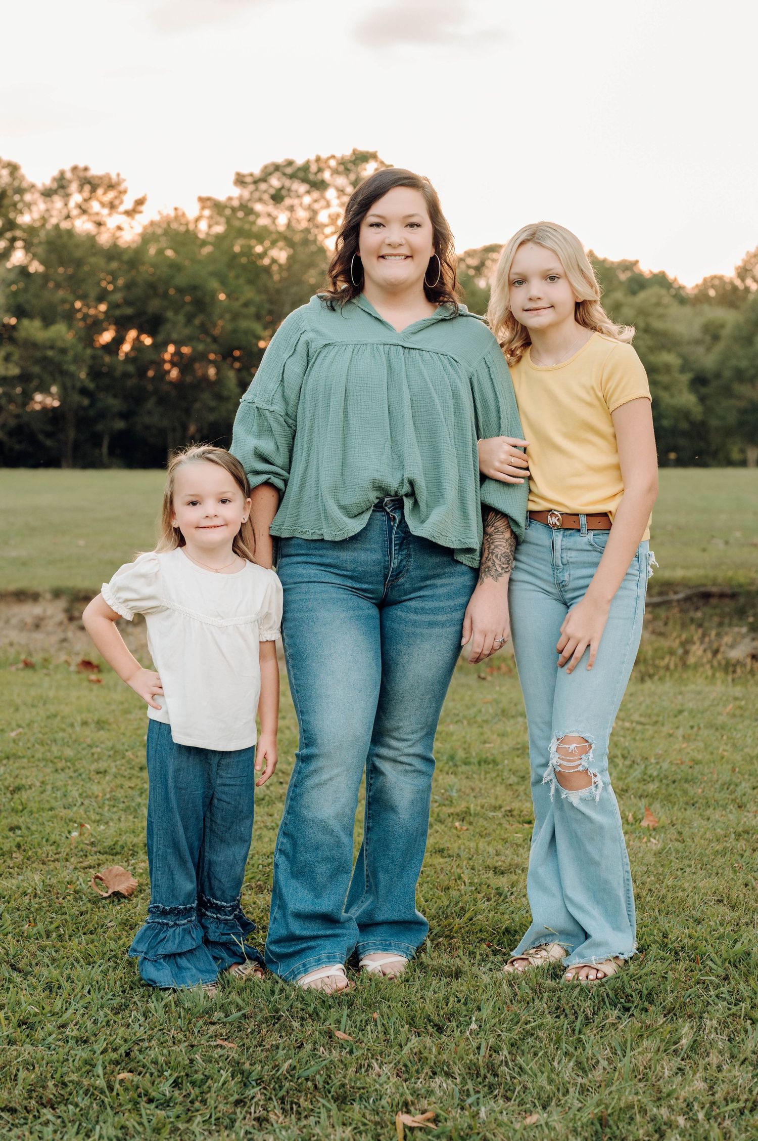 Family members wearing coordinated denim and casual attire pose together on grassy field at sunset.