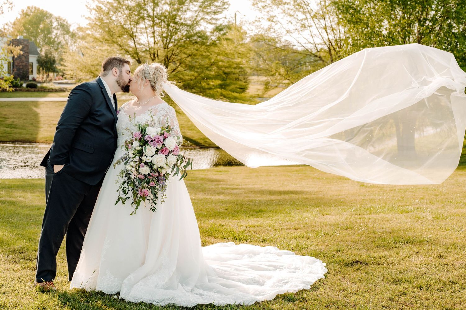 Romantic outdoor wedding portrait with dramatic flowing veil in natural setting.