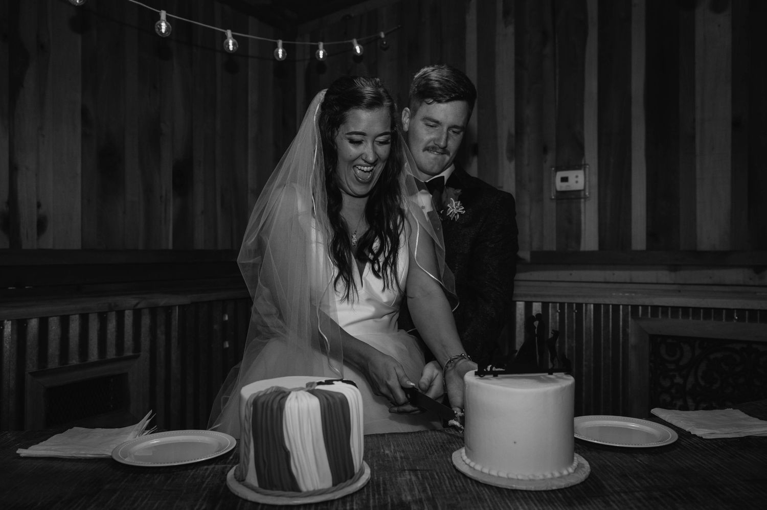 Black and white photo of couple cutting wedding cake together.