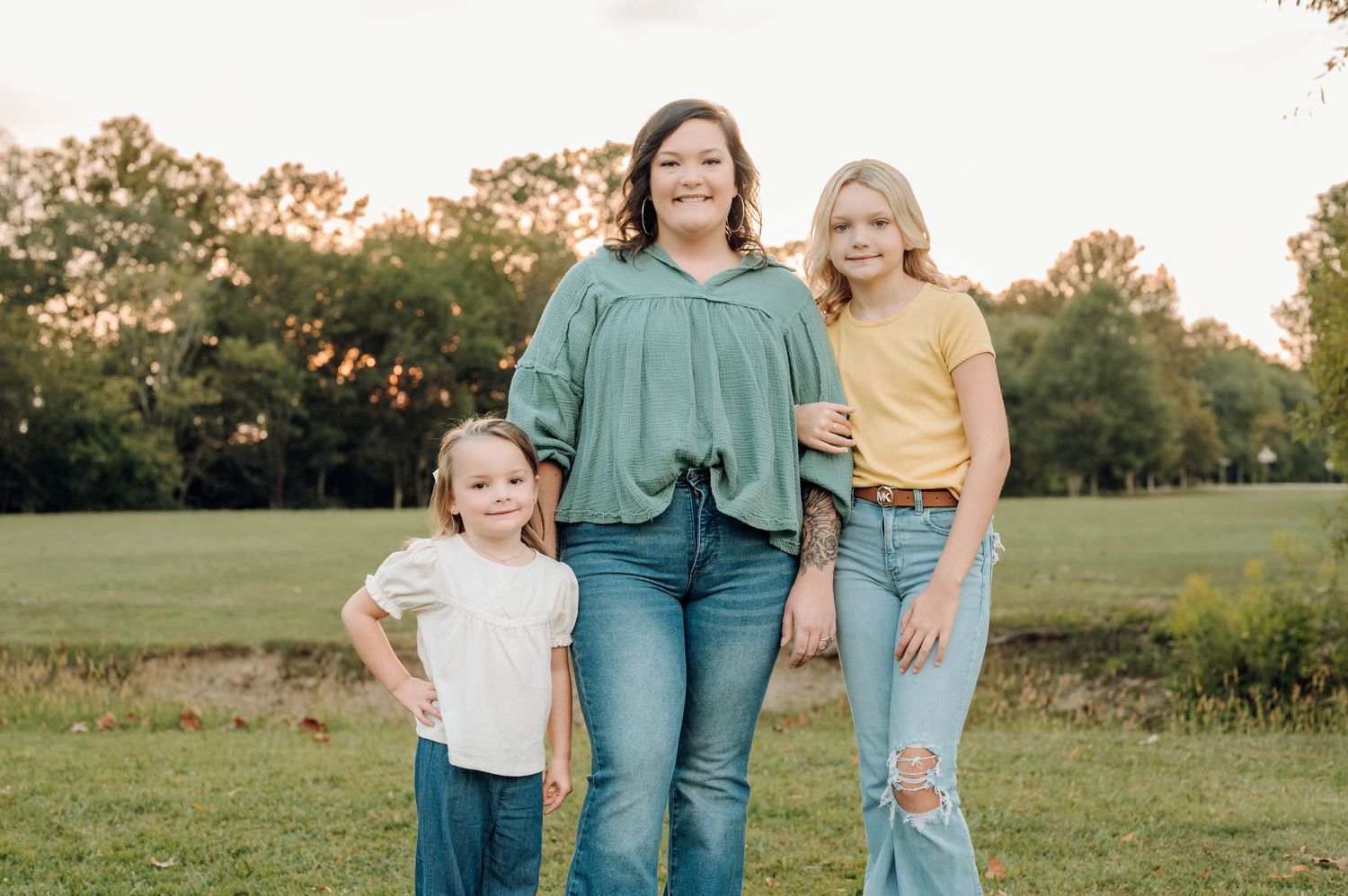 Three people stand together in a grassy field during golden hour sunset.