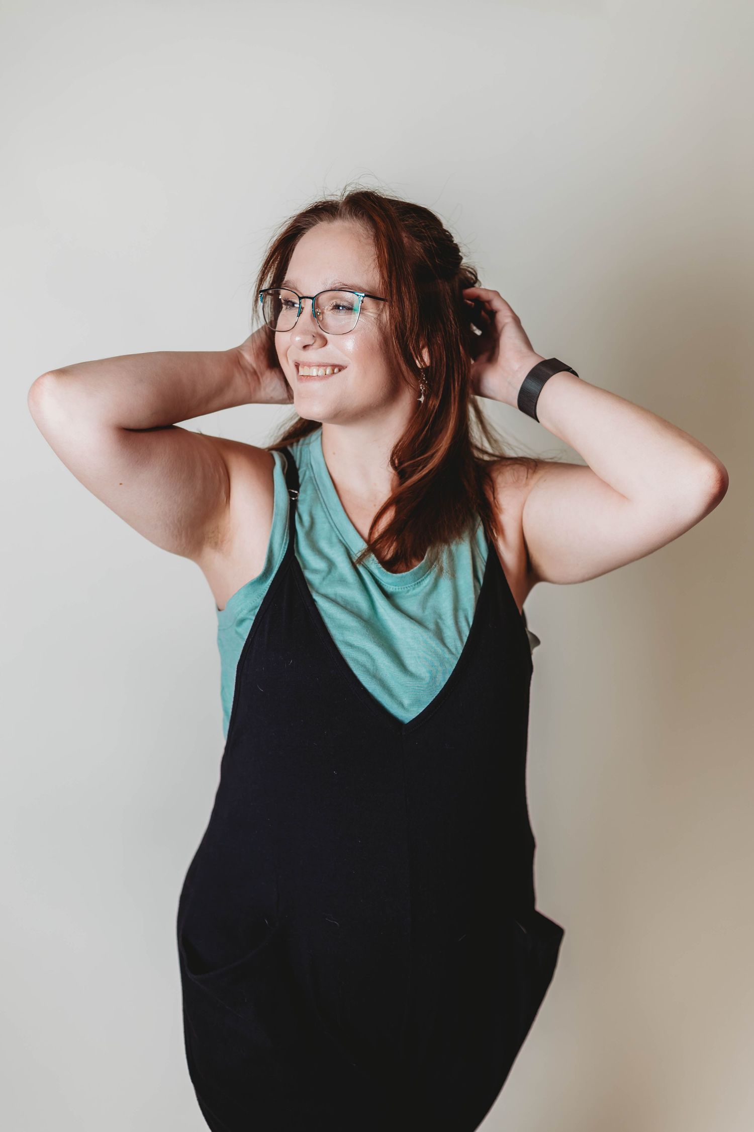 A person in a teal and black tank top poses against a neutral wall.