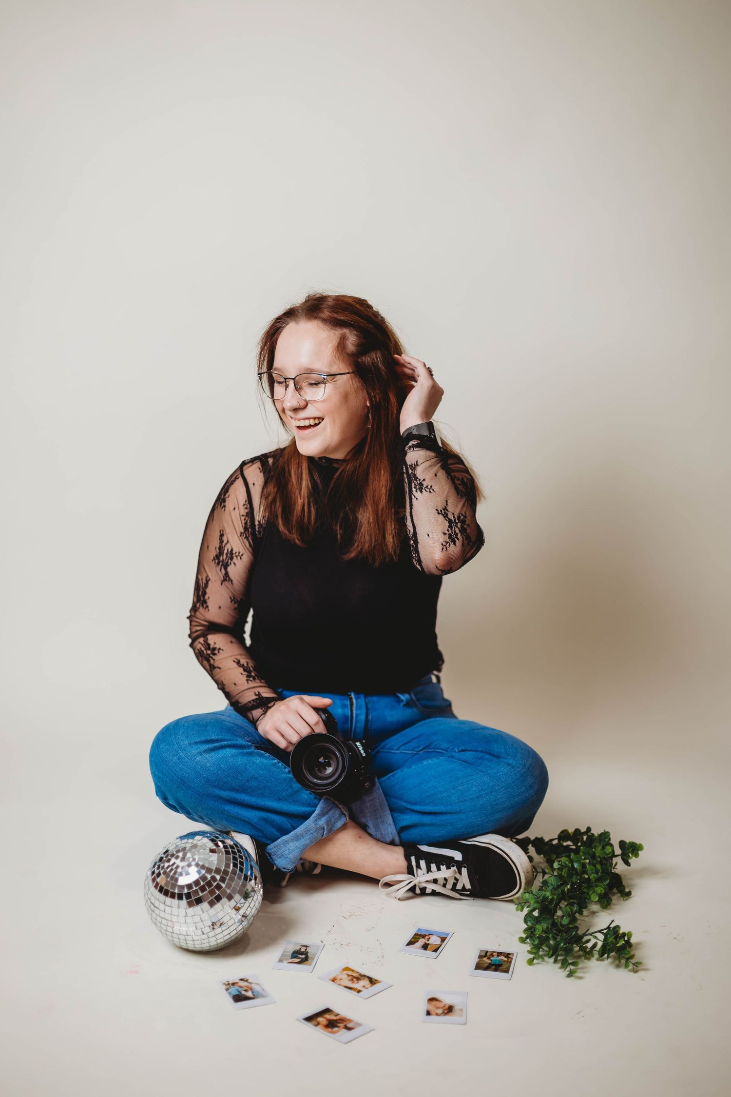 A photographer sits cross-legged with a camera, disco ball and scattered photos on white background.