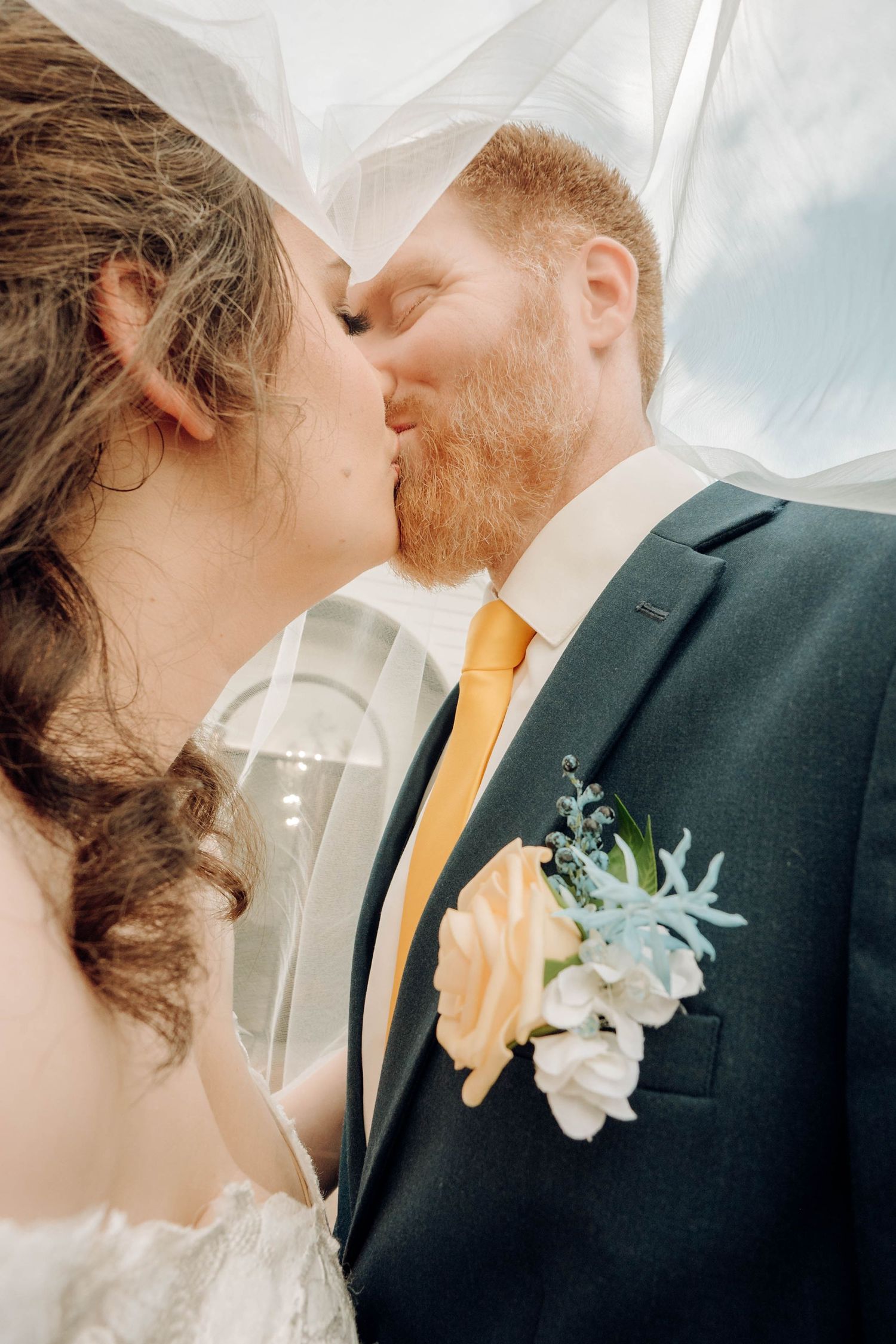 A romantic wedding moment captured under a flowing veil as the couple shares a tender kiss.
