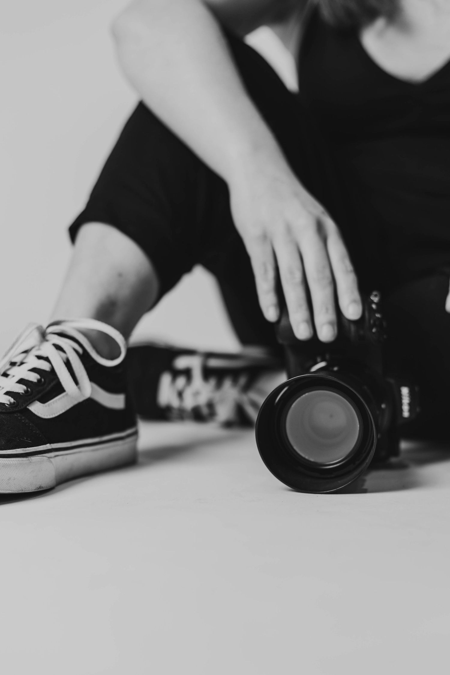 A black and white close-up shot of a Vans sneaker next to a camera lens on a light surface.