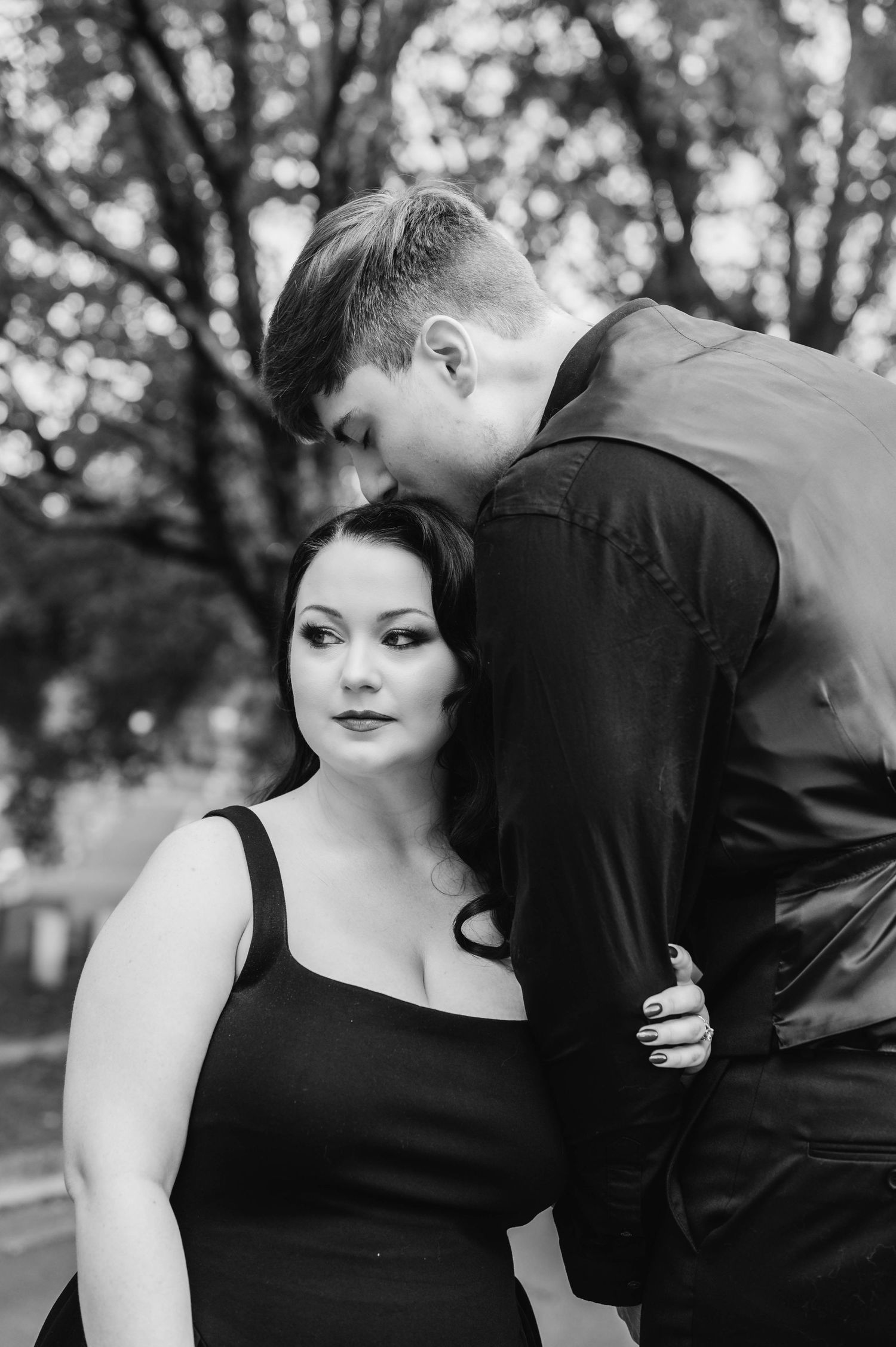 A romantic black and white photo series showing a couple in an intimate embrace outdoors among trees.