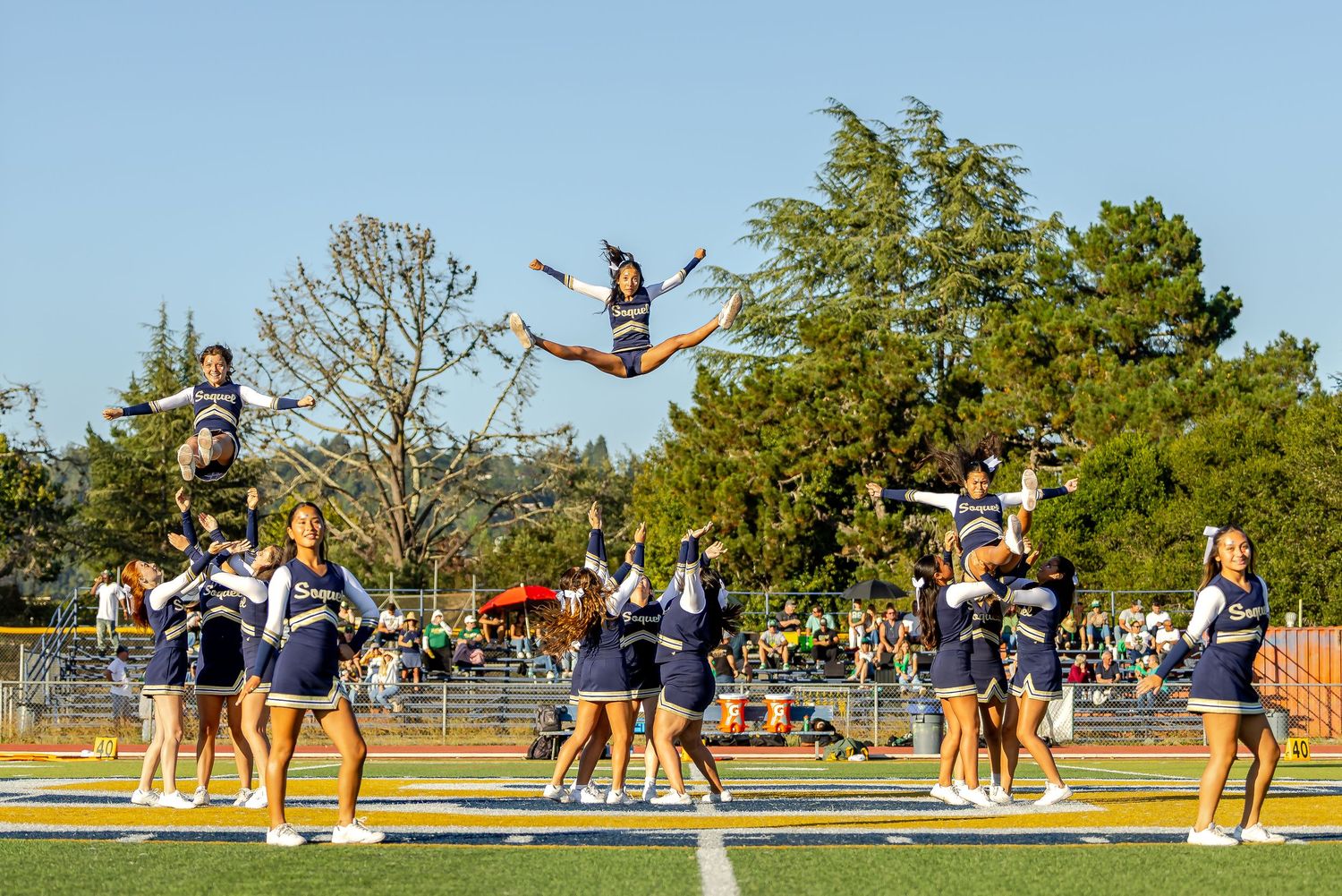 High school cheerleaders perform synchronized lifts and stunts during an outdoor practice session at a sports field.