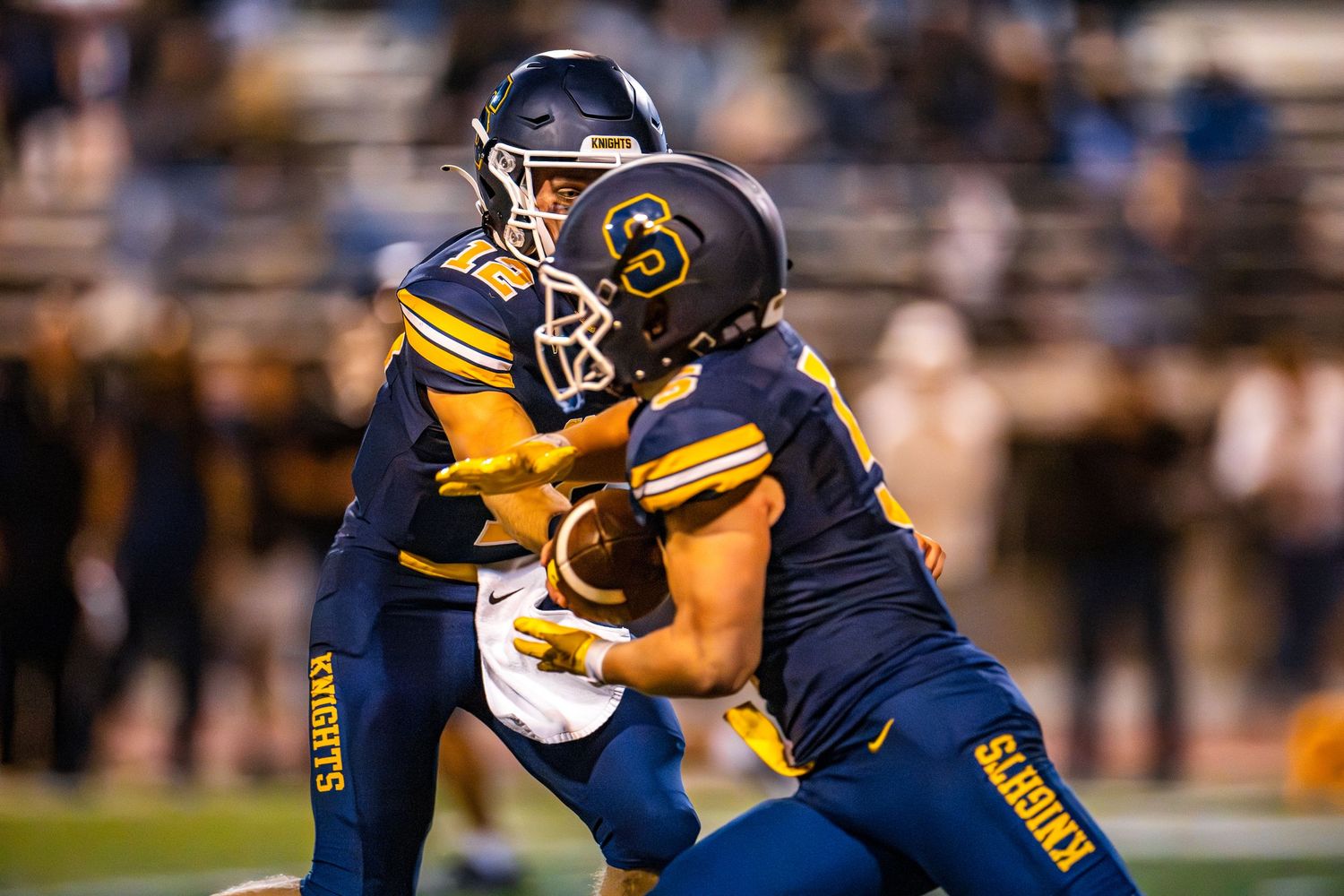 High school football players in navy and gold uniforms clash during an intense game play on the field.