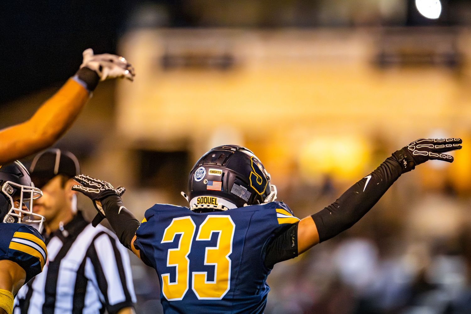 Football players in blue and gold uniforms celebrate with raised arms on the field during a game.